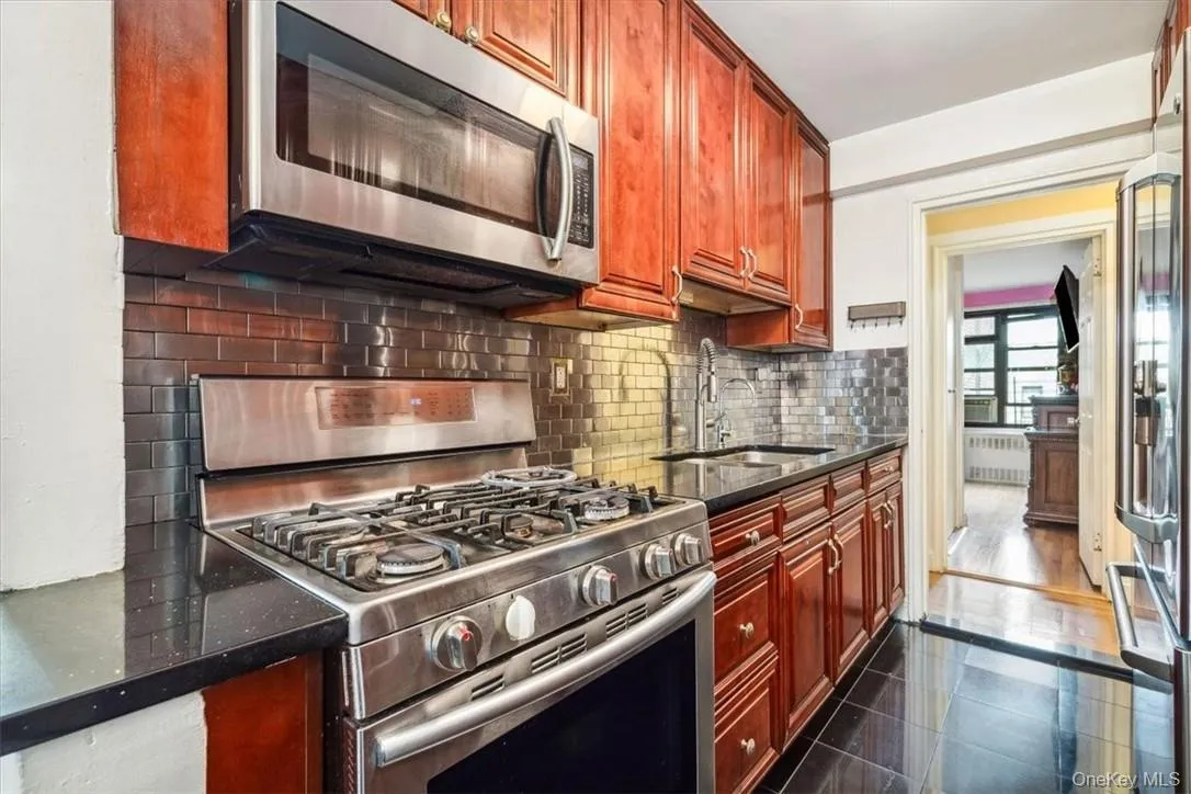 Kitchen with backsplash, dark tile flooring, radiator heating unit, appliances with stainless steel finishes, and sink Kitchen with backsplash, dark tile flooring, radiator heating unit, appliances with stainless steel finishes, and sink
