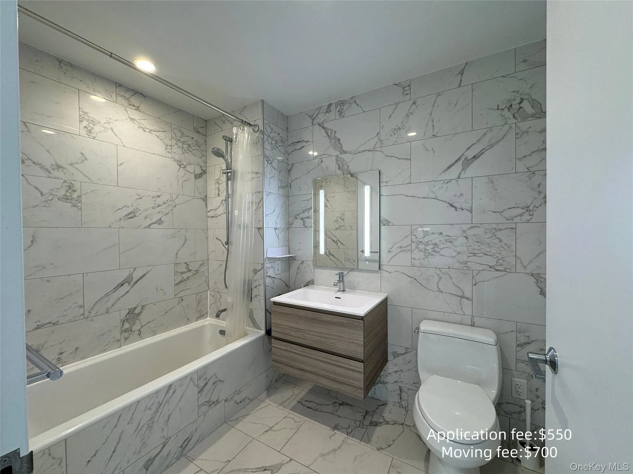 Full bathroom with vanity, a combined bath / shower with marble appearance, light marble finish floors, and tile walls Full bathroom with vanity, a combined bath / shower with marble appearance, light marble finish floors, and tile walls