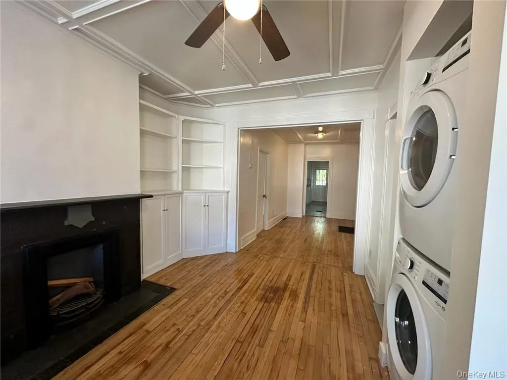 Living room with built in features, stacked washer and clothes dryer, ceiling fan, and light hardwood / wood-style floors Living room with built in features, stacked washer and clothes dryer, ceiling fan, and light hardwood / wood-style floors
