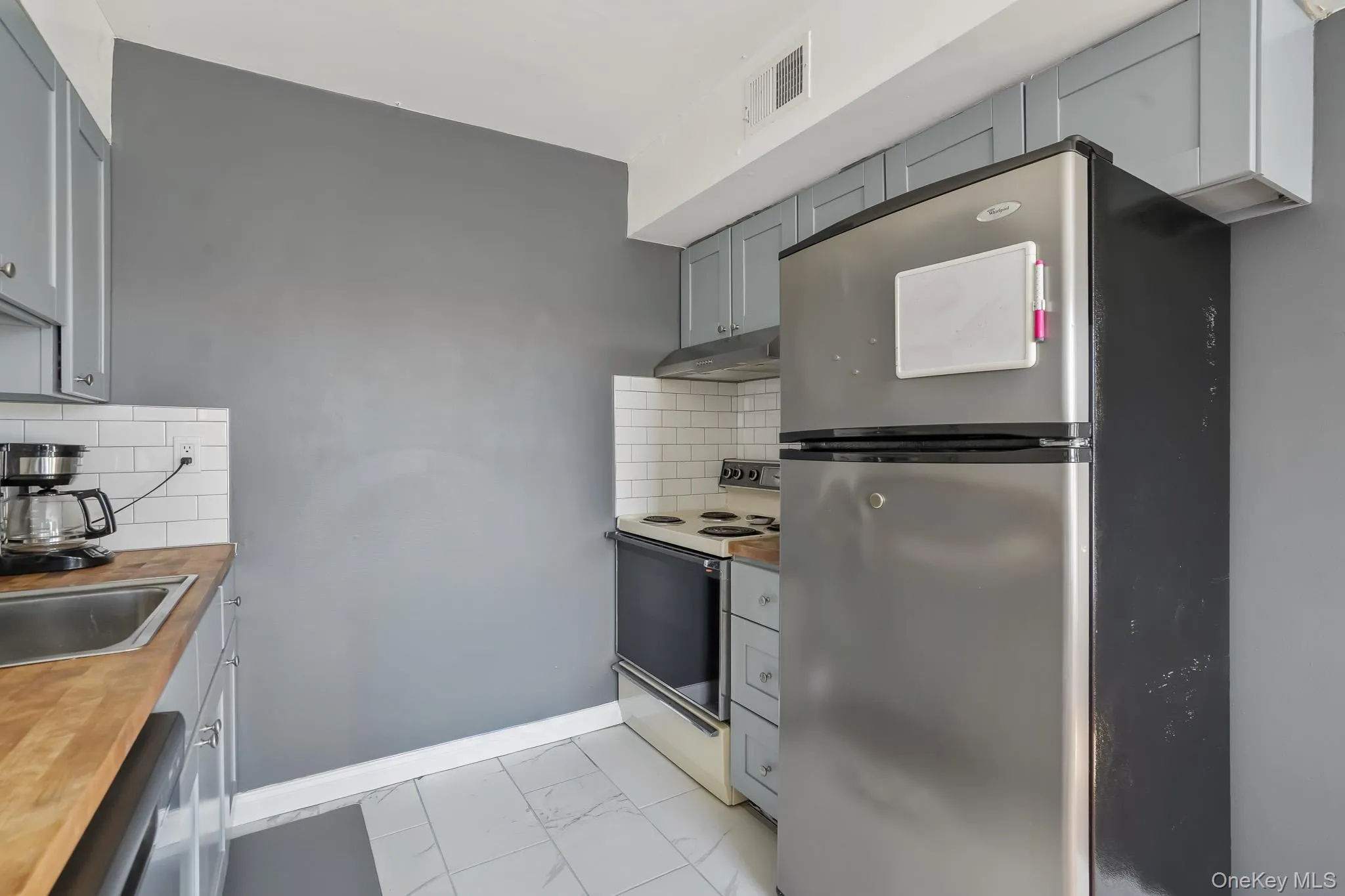 Kitchen with gray cabinets, freestanding refrigerator, white range with electric cooktop, and tasteful backsplash Kitchen with gray cabinets, freestanding refrigerator, white range with electric cooktop, and tasteful backsplash
