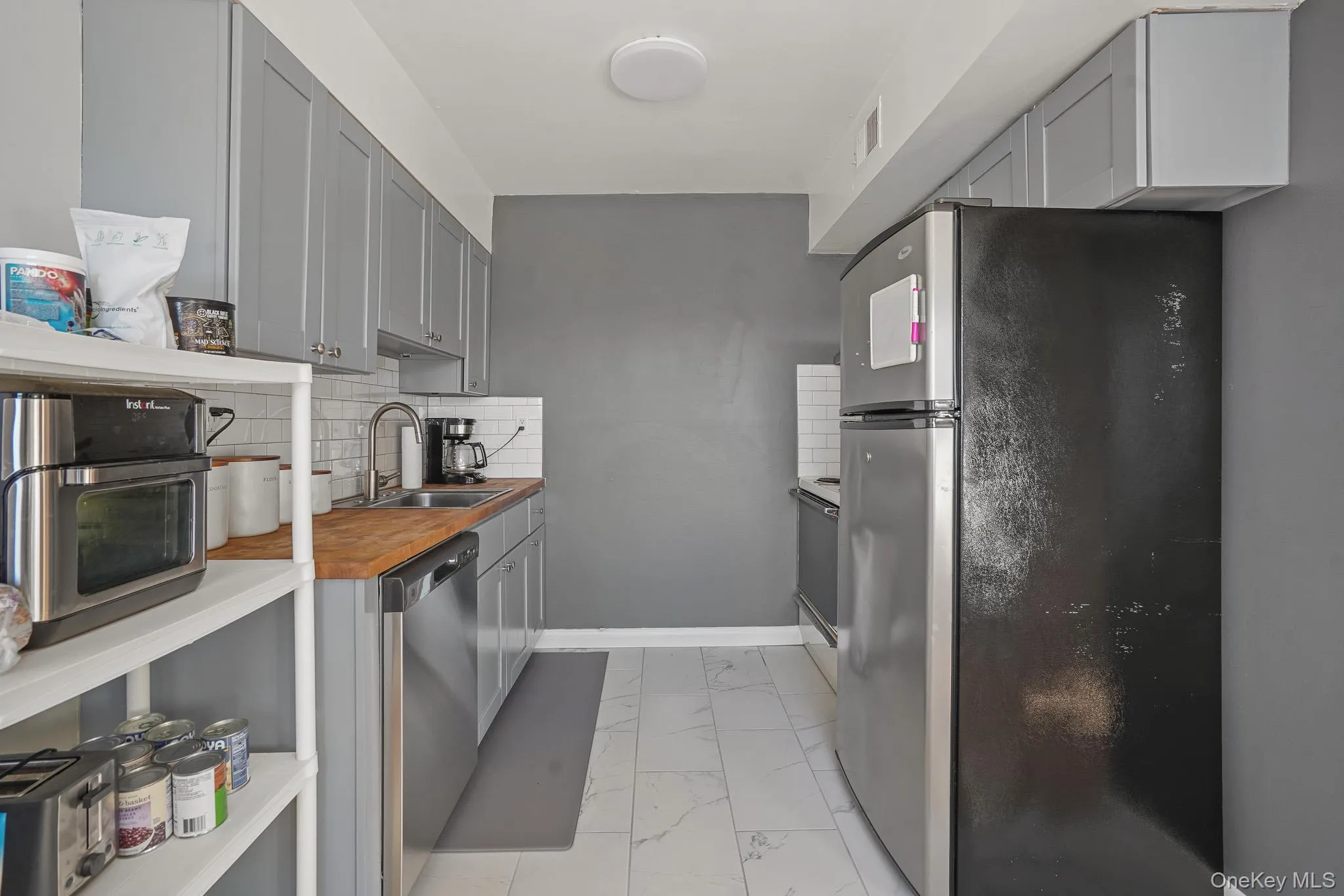 Kitchen with gray cabinetry, stainless steel appliances, light marble finish flooring, tasteful backsplash, and wooden counters Kitchen with gray cabinetry, stainless steel appliances, light marble finish flooring, tasteful backsplash, and wooden counters