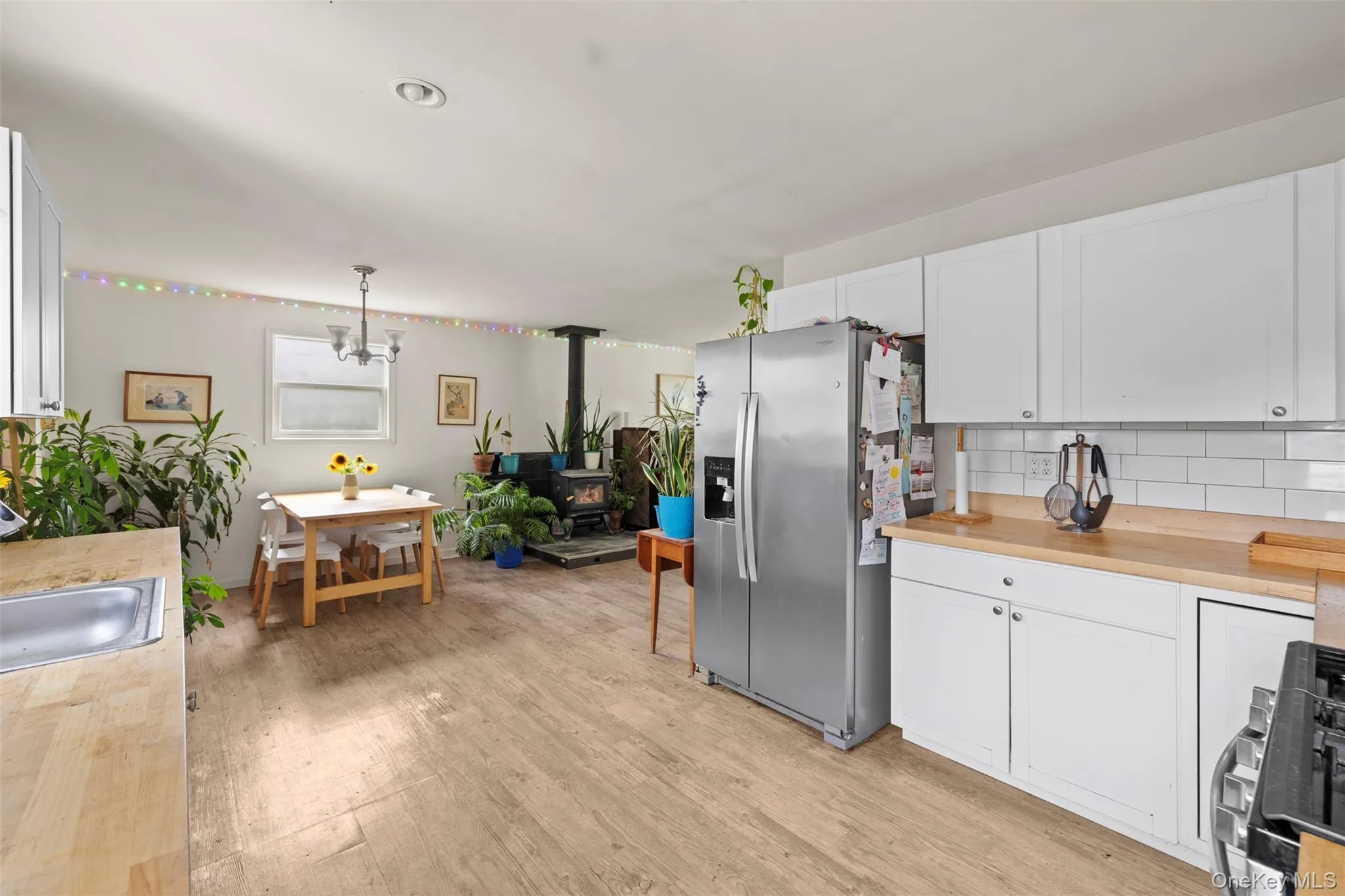 Kitchen featuring stainless steel fridge with ice dispenser, a wood stove, white cabinets, light wood-style floors, and backsplash Kitchen featuring stainless steel fridge with ice dispenser, a wood stove, white cabinets, light wood-style floors, and backsplash