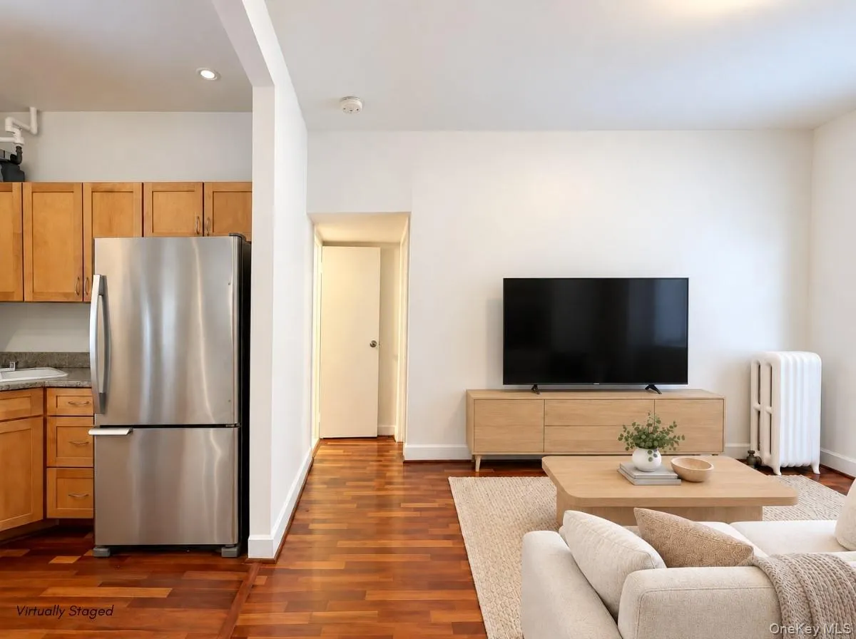 Wood-finish flooring throughout, stainless steel refrigerator, wood cabinetry, recessed lighting, and wall-mounted radiator Wood-finish flooring throughout, stainless steel refrigerator, wood cabinetry, recessed lighting, and wall-mounted radiator
