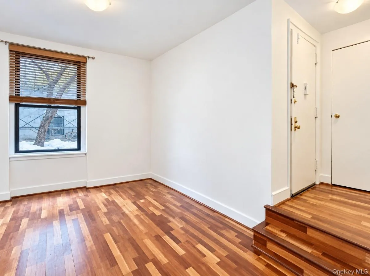 Wood-finish flooring throughout, bright white walls, and a window with wood-slat blinds Wood-finish flooring throughout, bright white walls, and a window with wood-slat blinds