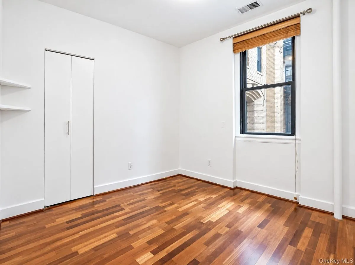 Warm wood-finish flooring, white walls, and a large window with a wood-slat blind Warm wood-finish flooring, white walls, and a large window with a wood-slat blind