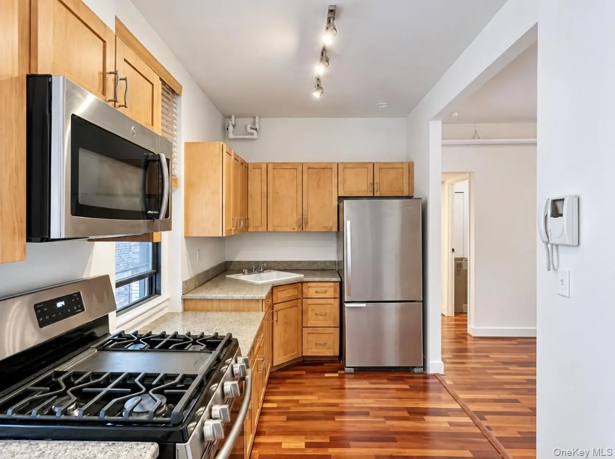 Kitchen featuring stainless steel appliances, wood-finish cabinetry, granite-style countertops, track lighting, and wood-finish flooring Kitchen featuring stainless steel appliances, wood-finish cabinetry, granite-style countertops, track lighting, and wood-finish flooring