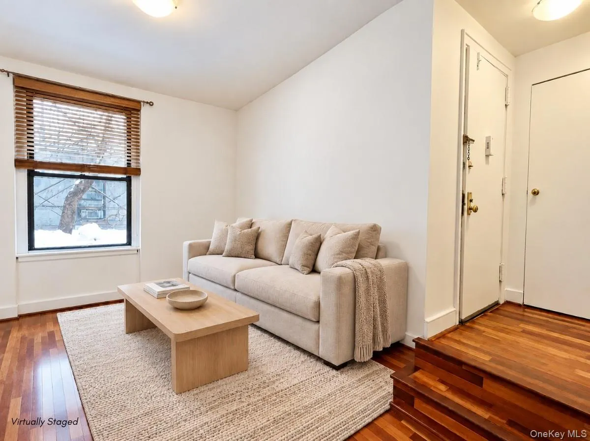 Hardwood flooring and crisp white walls define this living area, featuring a window with wood-finish blinds and a built-in light fixture Hardwood flooring and crisp white walls define this living area, featuring a window with wood-finish blinds and a built-in light fixture