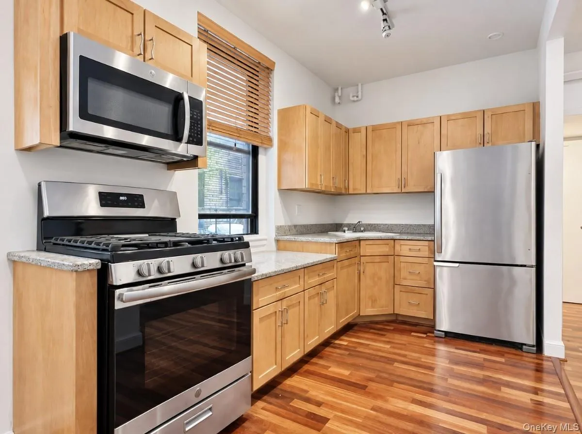 Kitchen featuring wood-finish flooring, light wood cabinetry, stainless steel appliances, and stone countertops Kitchen featuring wood-finish flooring, light wood cabinetry, stainless steel appliances, and stone countertops