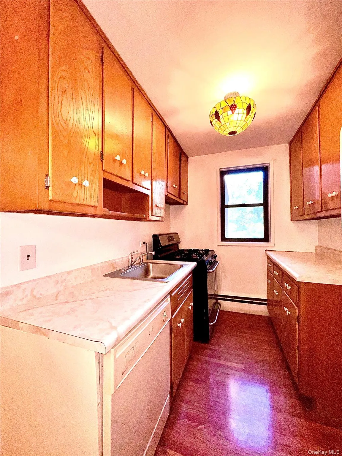 Kitchen with black gas stove, light countertops, dishwasher, brown cabinetry, and dark wood-style flooring Kitchen with black gas stove, light countertops, dishwasher, brown cabinetry, and dark wood-style flooring