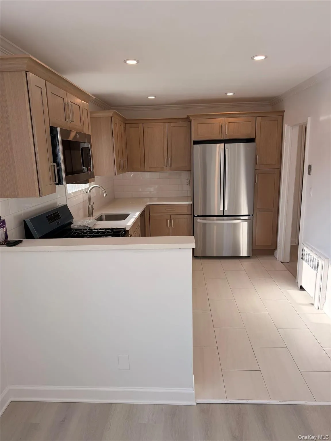 Kitchen with stainless steel appliances, crown molding, tasteful backsplash, radiator, and recessed lighting Kitchen with stainless steel appliances, crown molding, tasteful backsplash, radiator, and recessed lighting