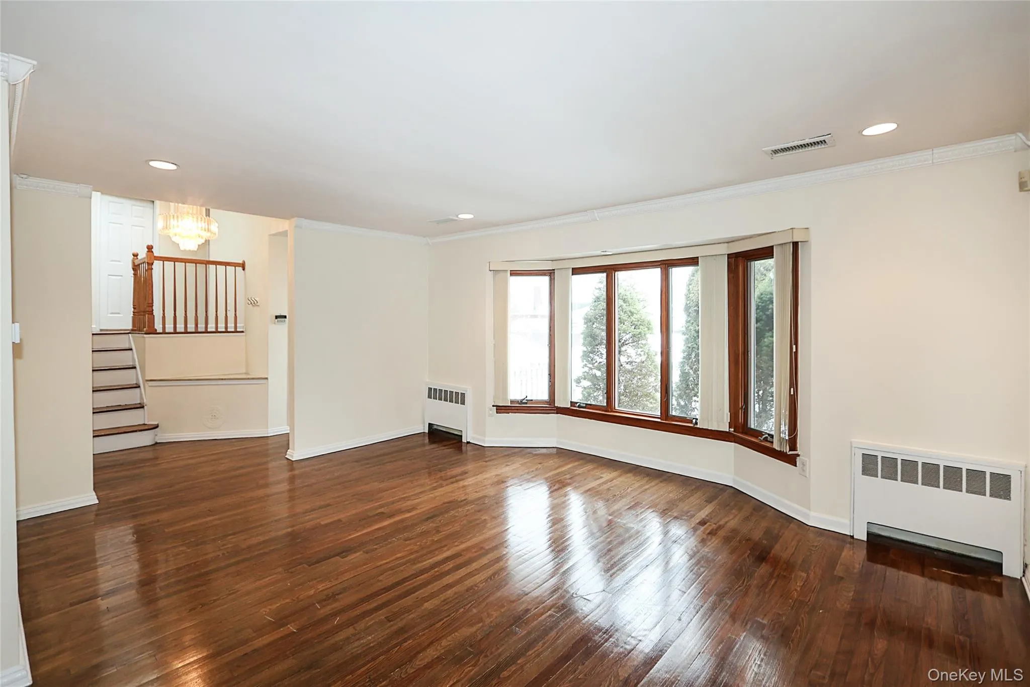 Unfurnished living room featuring radiator heating unit, dark wood-style flooring, crown molding, and recessed lighting Unfurnished living room featuring radiator heating unit, dark wood-style flooring, crown molding, and recessed lighting