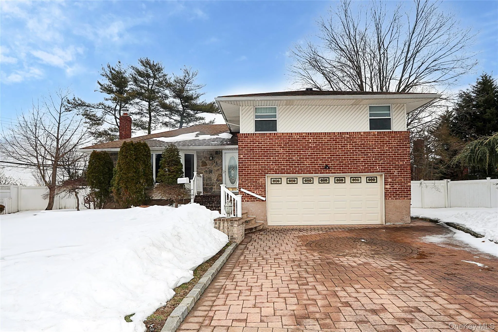 Tri-level home with an attached garage, decorative driveway, brick siding, and a chimney Tri-level home with an attached garage, decorative driveway, brick siding, and a chimney
