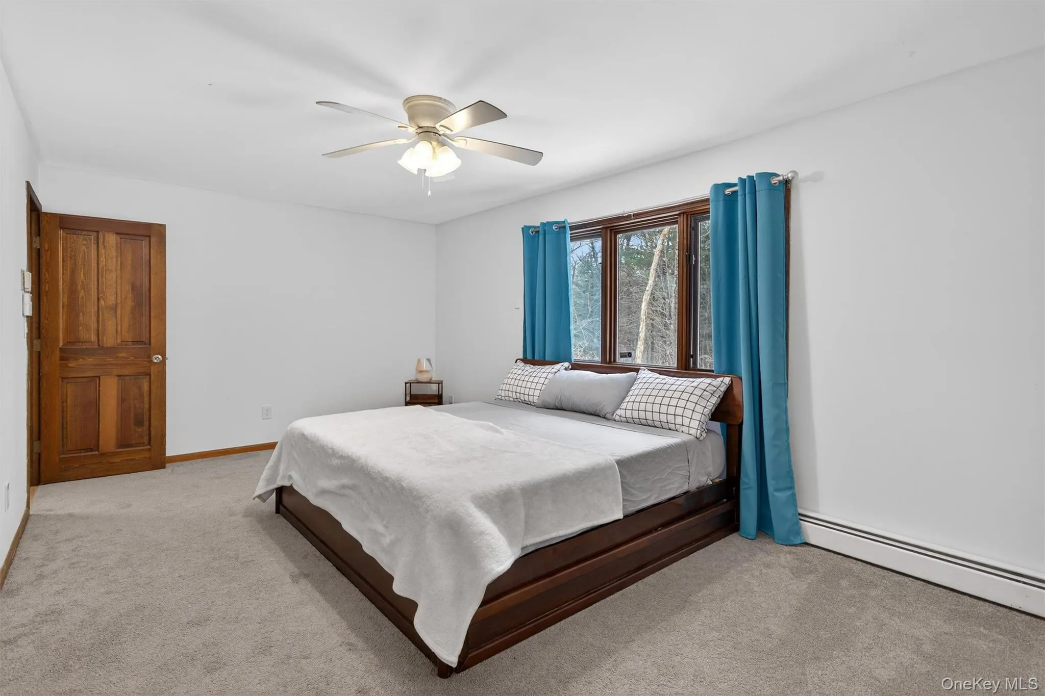 Bedroom with light carpet, ceiling fan, and a baseboard heating unit Bedroom with light carpet, ceiling fan, and a baseboard heating unit