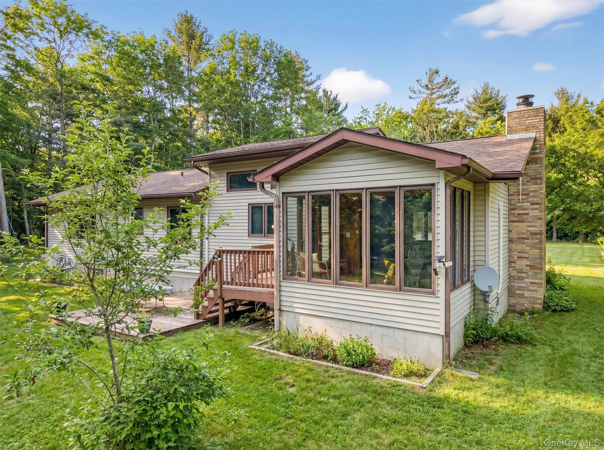 Back of property with a chimney, a yard, a sunroom, and a deck Back of property with a chimney, a yard, a sunroom, and a deck
