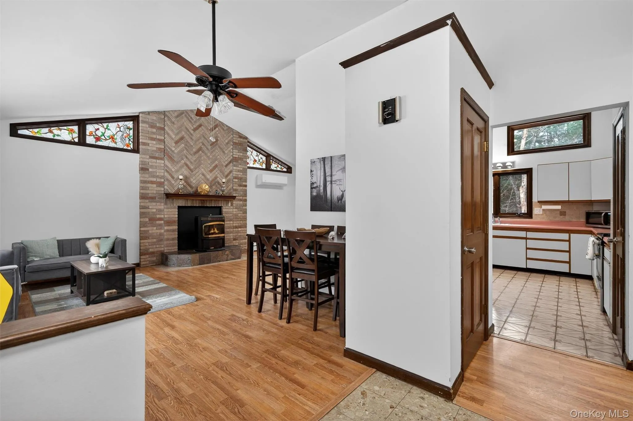 Living room with light wood-style flooring, ceiling fan, lofted ceiling, and a wood stove Living room with light wood-style flooring, ceiling fan, lofted ceiling, and a wood stove
