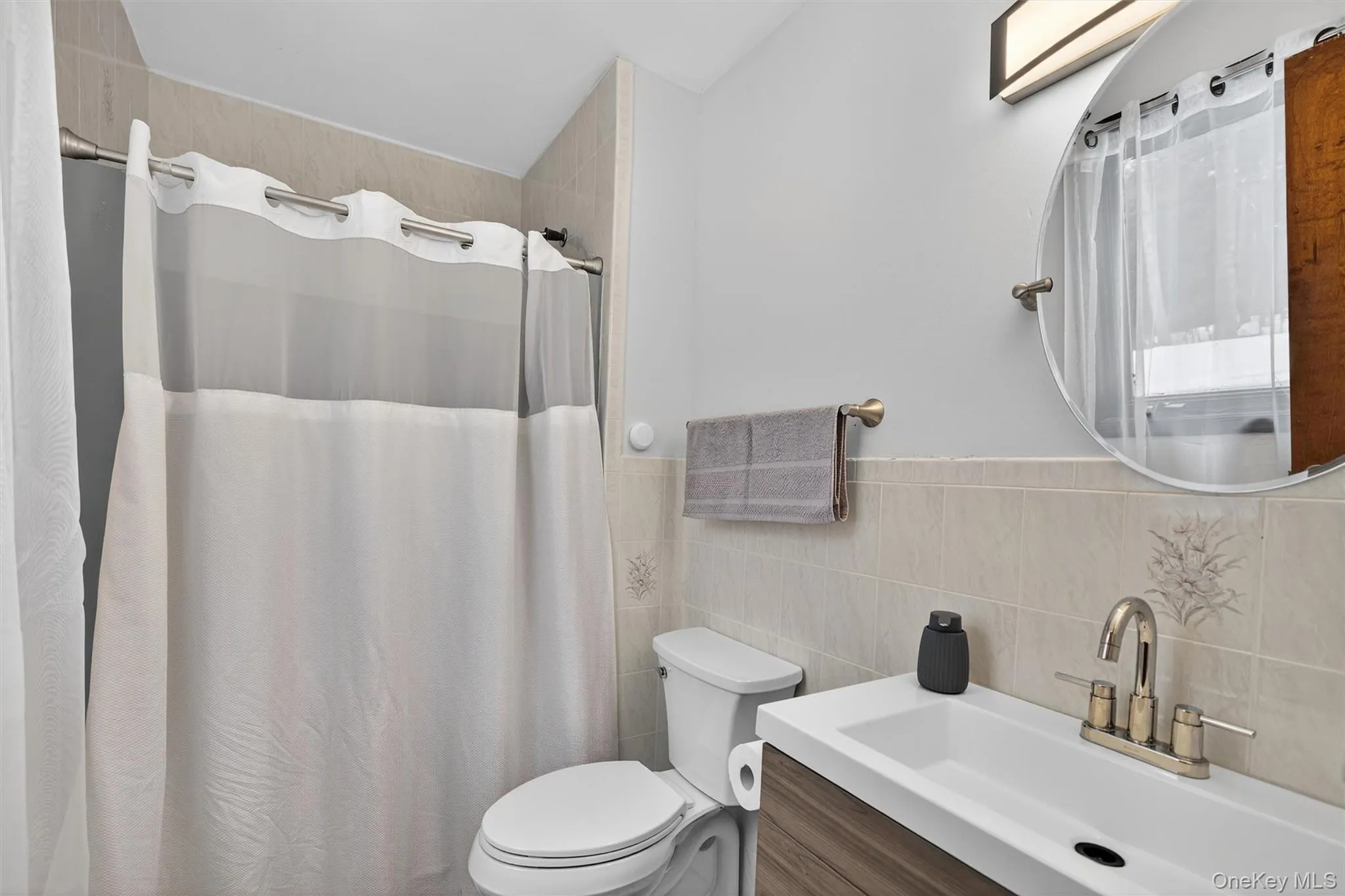 Full bath featuring curtained shower, vanity, tile walls, and a wainscoted wall Full bath featuring curtained shower, vanity, tile walls, and a wainscoted wall