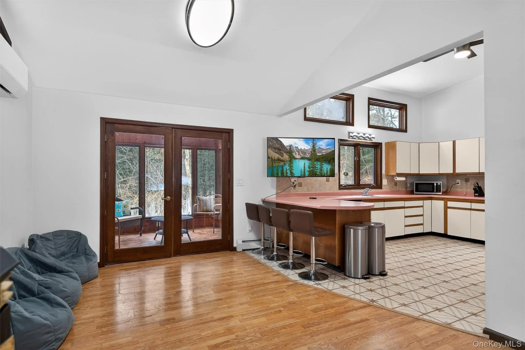 Dual tone kitchen featuring a breakfast bar, french doors, light wood-type flooring, light countertops, and lofted ceiling Dual tone kitchen featuring a breakfast bar, french doors, light wood-type flooring, light countertops, and lofted ceiling