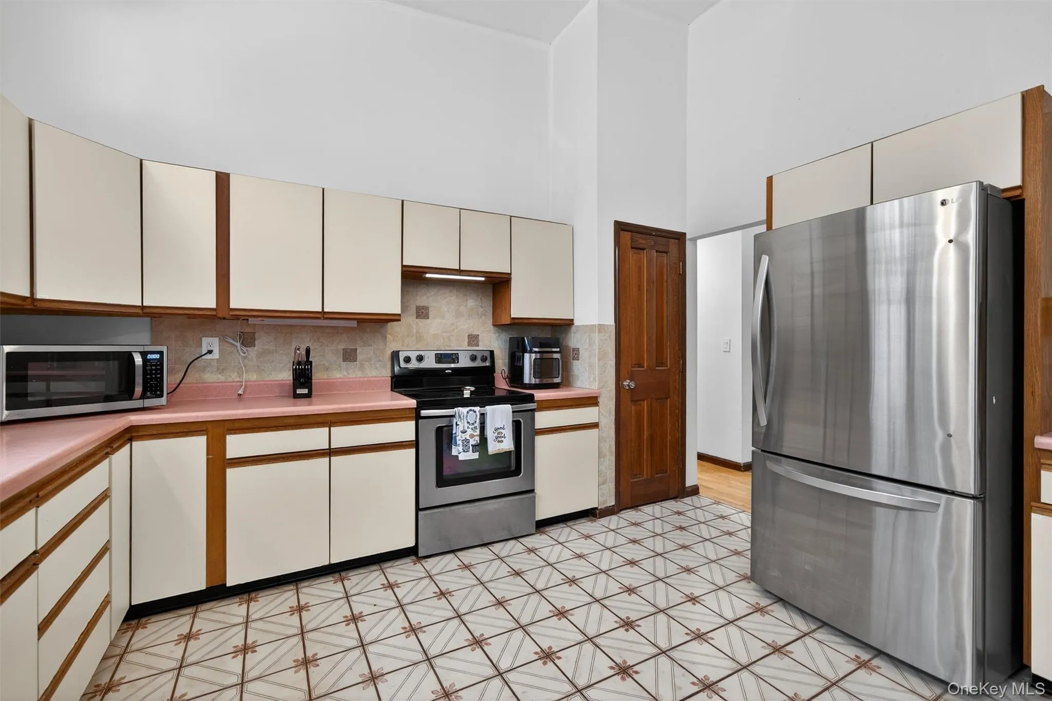 Kitchen with two tone color scheme, stainless steel appliances, light countertops, a high ceiling, and tasteful backsplash Kitchen with two tone color scheme, stainless steel appliances, light countertops, a high ceiling, and tasteful backsplash