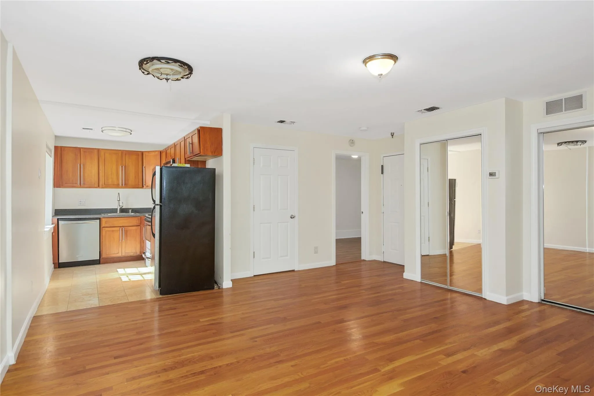 Kitchen featuring freestanding refrigerator, brown cabinets, light wood-style floors, and stainless steel dishwasher Kitchen featuring freestanding refrigerator, brown cabinets, light wood-style floors, and stainless steel dishwasher