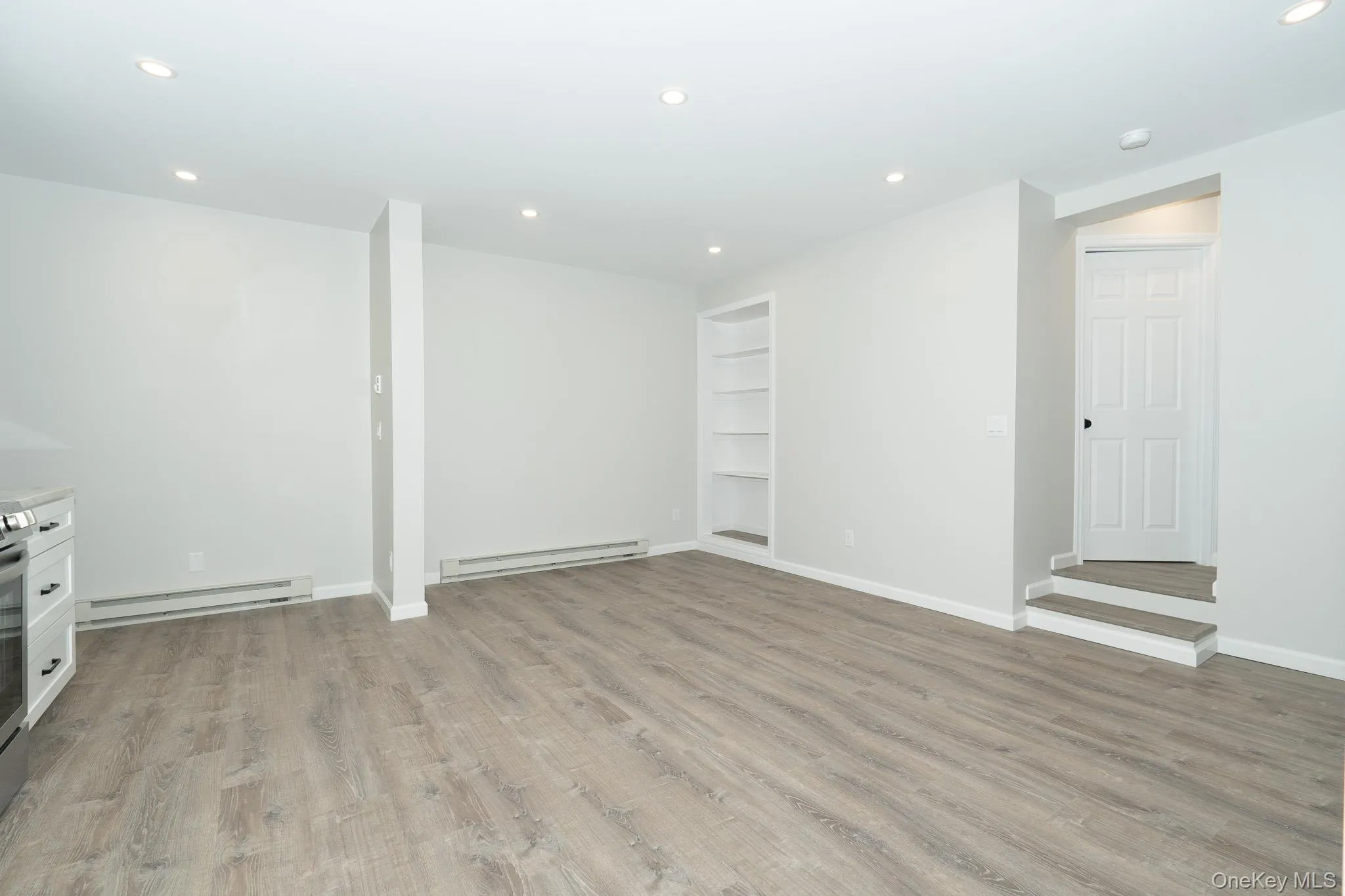 Below grade area featuring a baseboard radiator, light wood-type flooring, and built in features Below grade area featuring a baseboard radiator, light wood-type flooring, and built in features