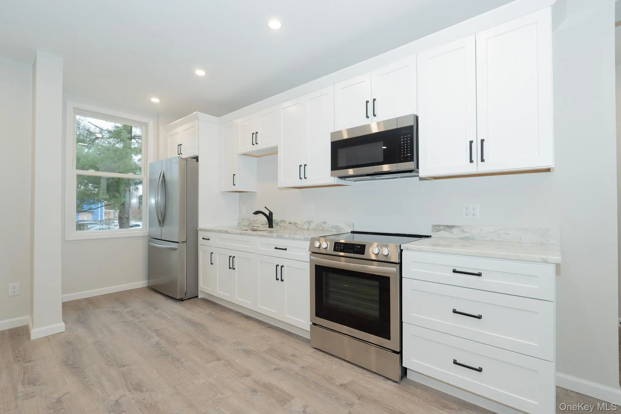 Kitchen featuring white cabinetry, stainless steel appliances, baseboards, light wood finished floors, and light stone countertops Kitchen featuring white cabinetry, stainless steel appliances, baseboards, light wood finished floors, and light stone countertops