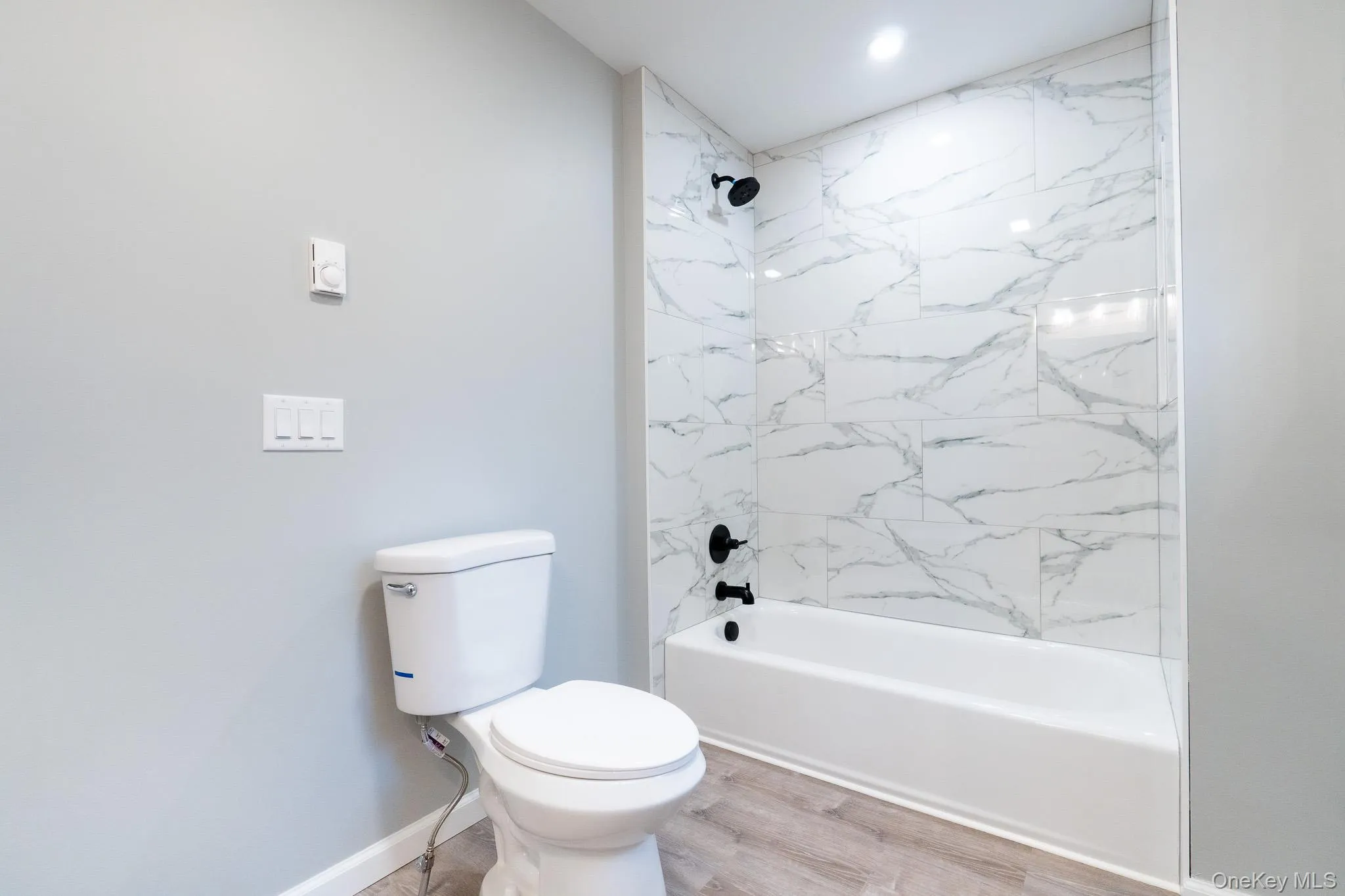 Full bathroom with toilet, tub / shower combination, baseboards, and wood finished floors Full bathroom with toilet, tub / shower combination, baseboards, and wood finished floors