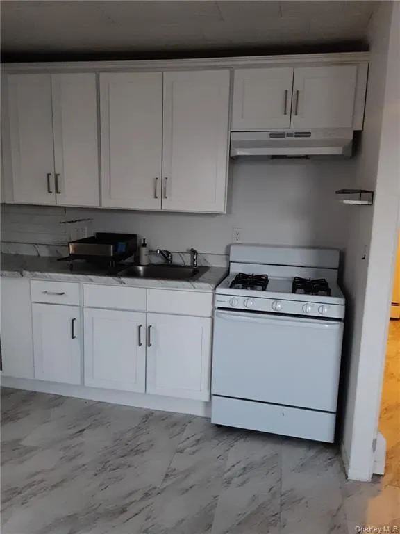 Kitchen featuring white gas range, white cabinetry, and light marble finish floors Kitchen featuring white gas range, white cabinetry, and light marble finish floors