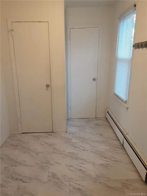 Corridor featuring a baseboard heating unit and light marble finish flooring Corridor featuring a baseboard heating unit and light marble finish flooring