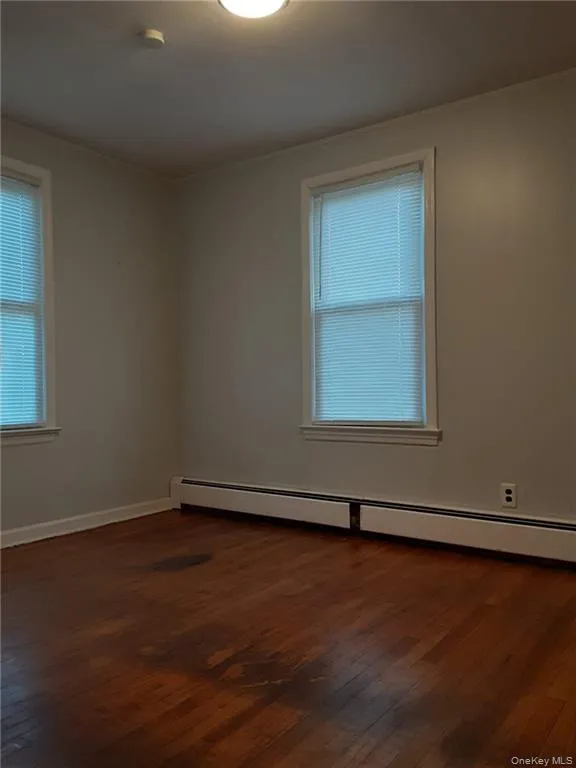 Empty room featuring a baseboard heating unit and dark wood-style flooring Empty room featuring a baseboard heating unit and dark wood-style flooring