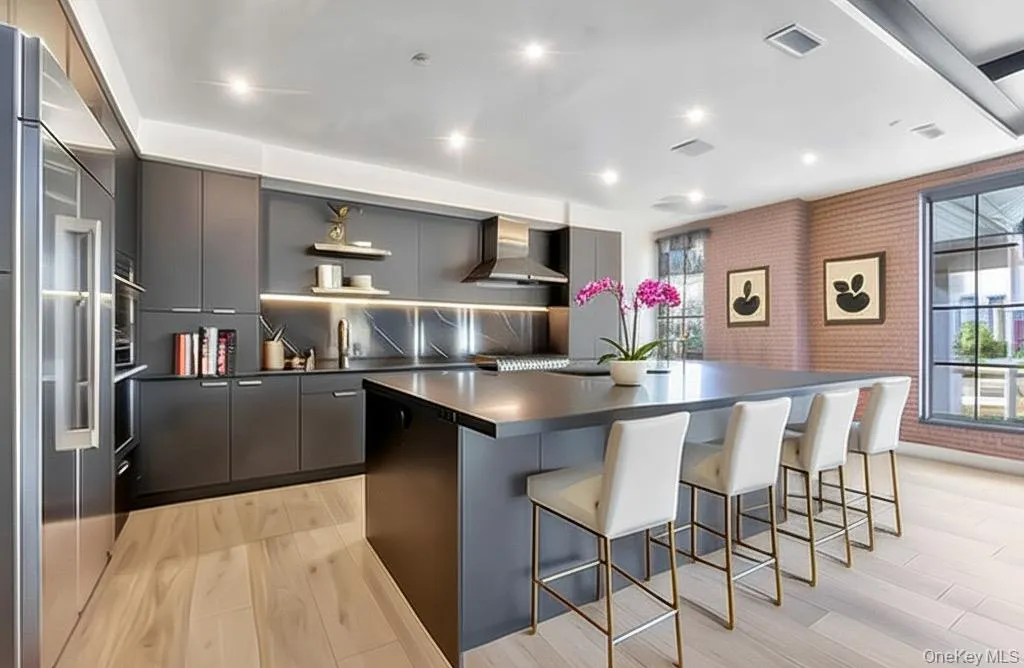Kitchen with dark countertops, wall chimney exhaust hood, modern cabinets, a center island, and recessed lighting Kitchen with dark countertops, wall chimney exhaust hood, modern cabinets, a center island, and recessed lighting