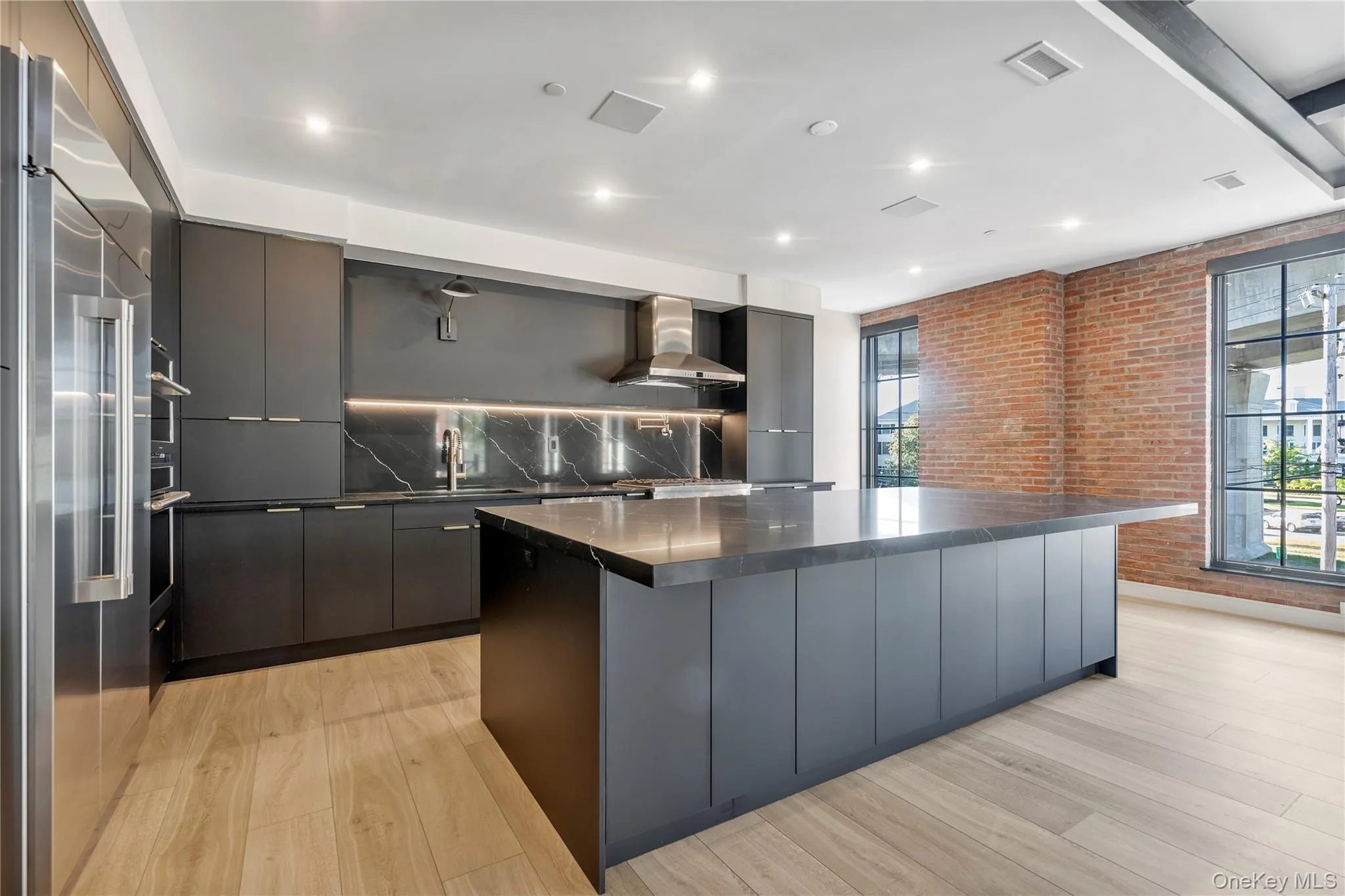 Kitchen with wall chimney range hood, high quality fridge, modern cabinets, brick wall, and a spacious island Kitchen with wall chimney range hood, high quality fridge, modern cabinets, brick wall, and a spacious island