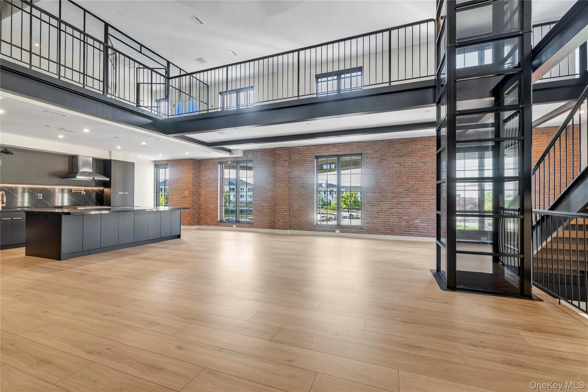 Unfurnished living room featuring a towering ceiling with magnificent black iron fan, brick wall, stairs, and light wood-style floors Unfurnished living room featuring a towering ceiling with magnificent black iron fan, brick wall, stairs, and light wood-style floors