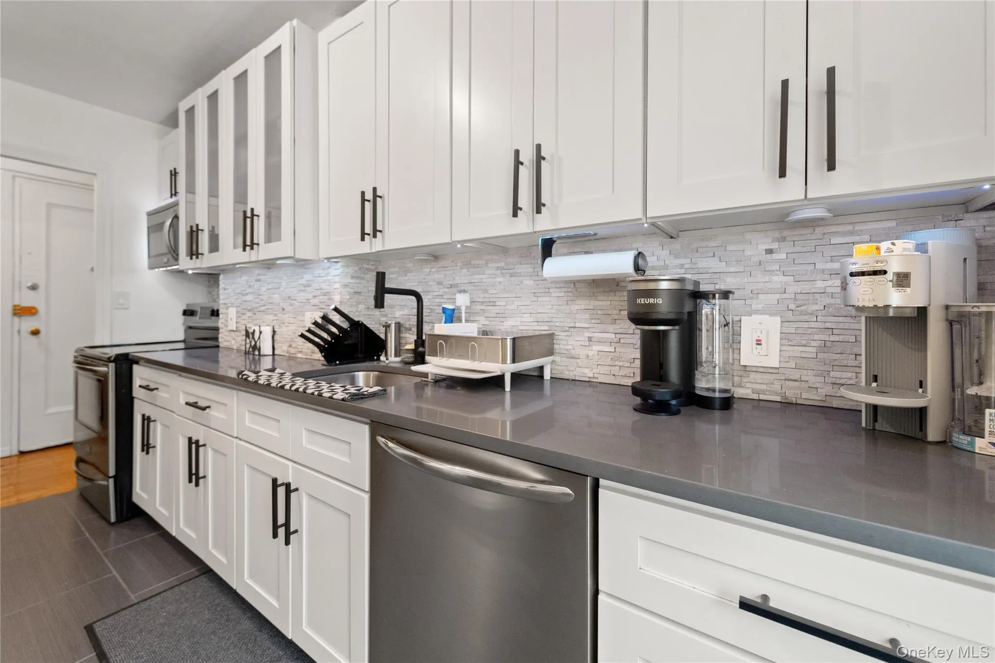 Kitchen with stainless steel appliances, white cabinets, glass insert cabinets, and tasteful backsplash Kitchen with stainless steel appliances, white cabinets, glass insert cabinets, and tasteful backsplash