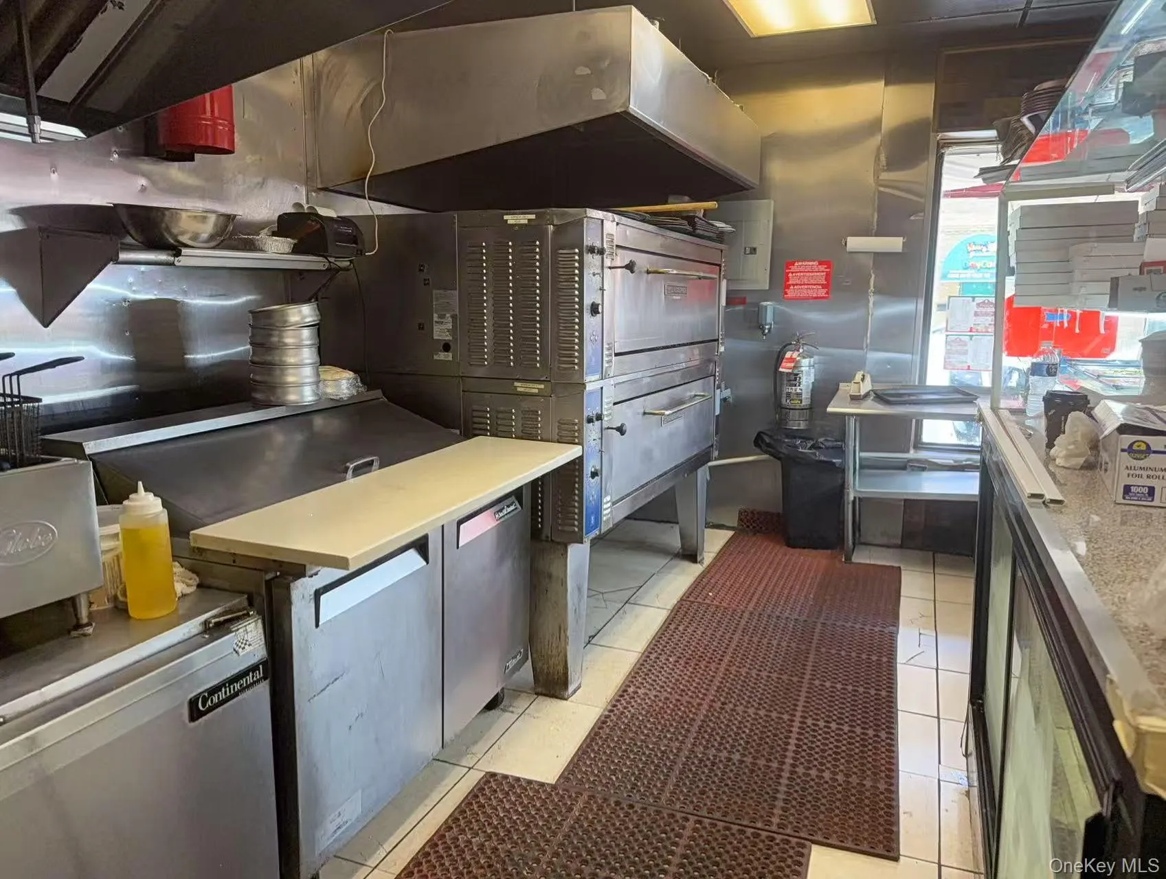 Kitchen with ventilation hood, light tile patterned flooring, light countertops, and electric panel Kitchen with ventilation hood, light tile patterned flooring, light countertops, and electric panel