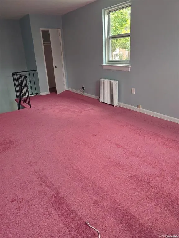 Carpeted empty room featuring radiator heating unit and baseboards Carpeted empty room featuring radiator heating unit and baseboards
