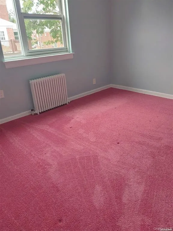 Spare room featuring radiator, healthy amount of natural light, and carpet flooring Spare room featuring radiator, healthy amount of natural light, and carpet flooring