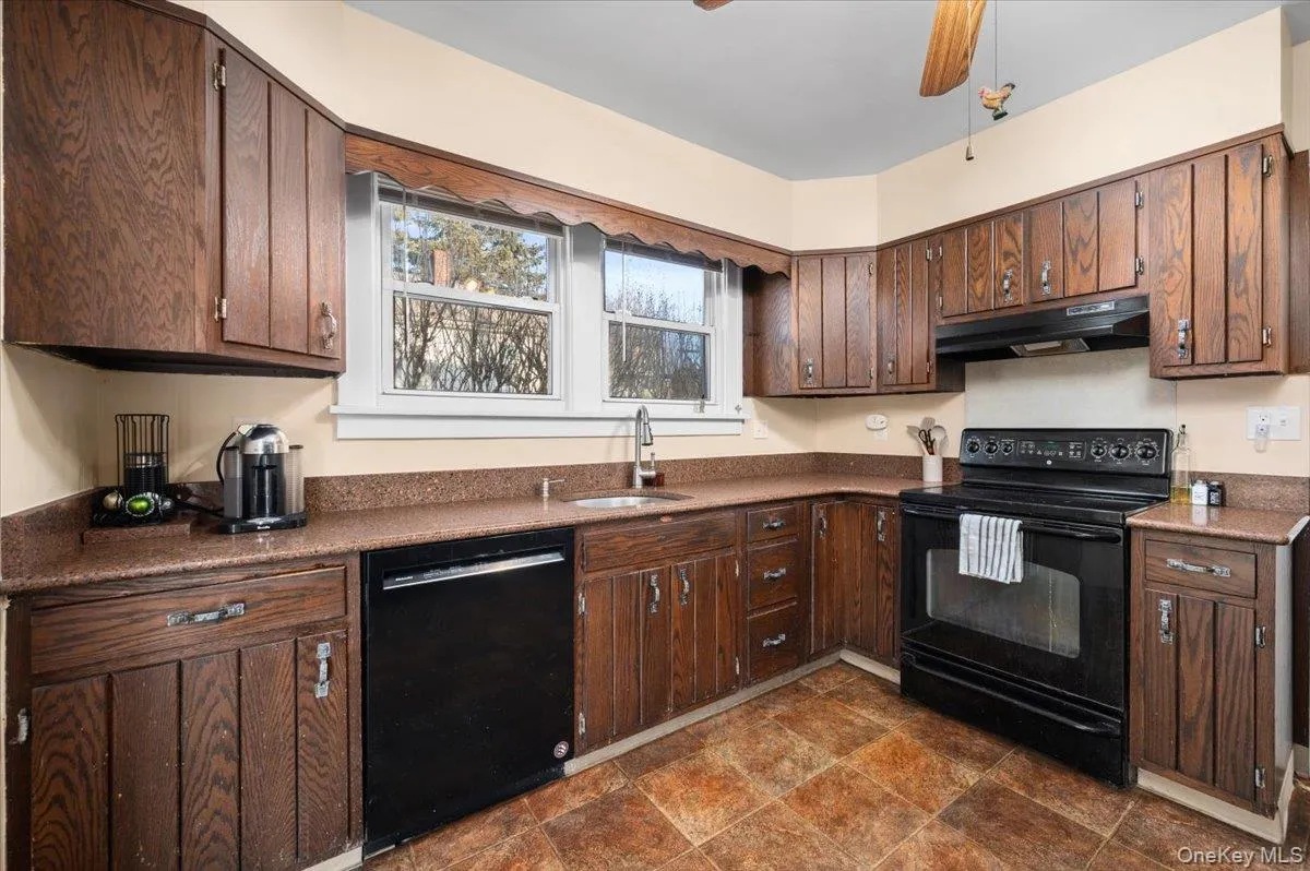 Kitchen featuring black appliances, dark wood finish cabinets, stone finish floors, and a ceiling fan Kitchen featuring black appliances, dark wood finish cabinets, stone finish floors, and a ceiling fan