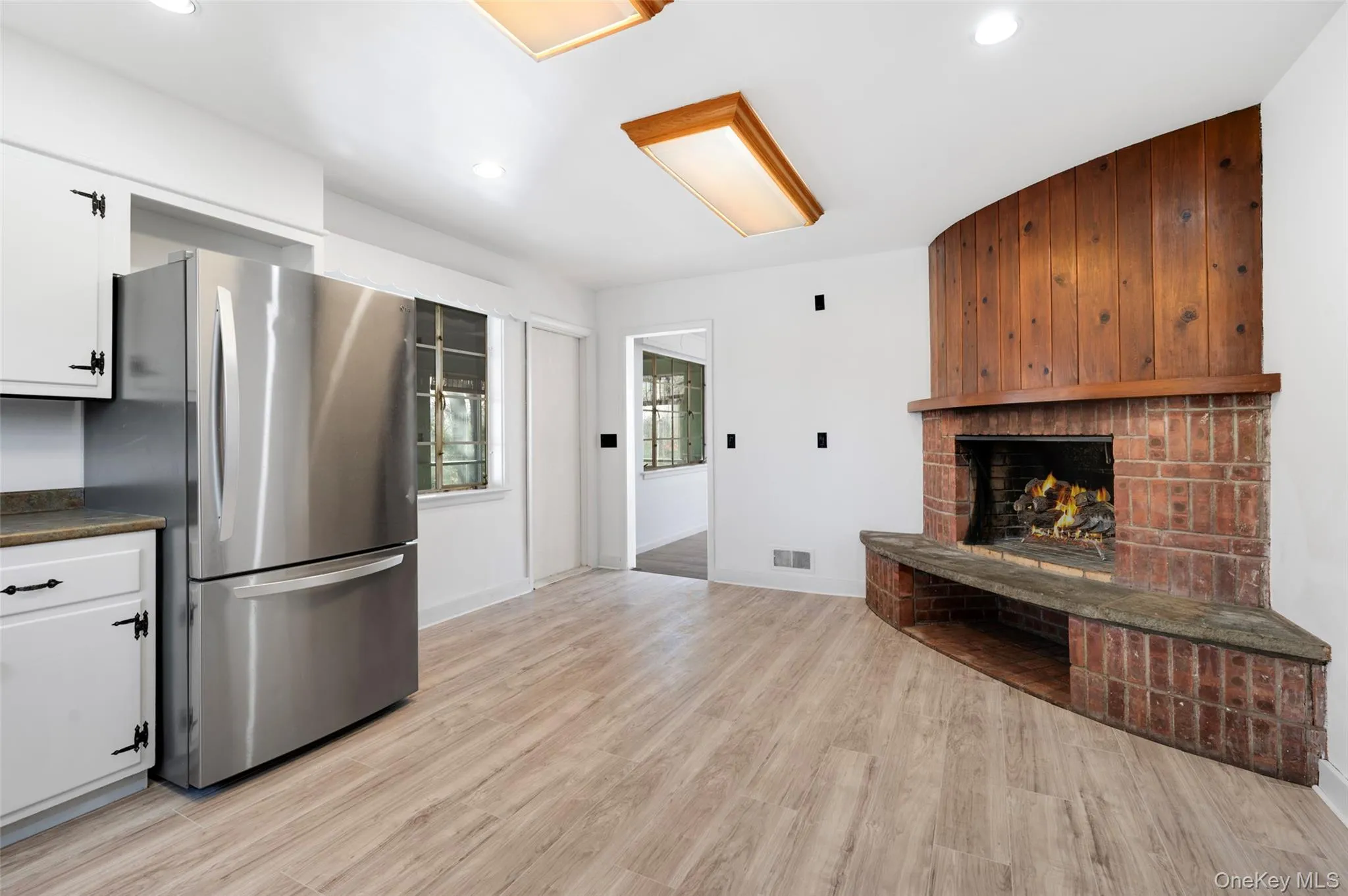 Kitchen featuring white cabinetry, a fireplace, stainless steel refrigerator, and light hardwood / wood-style flooring Kitchen featuring white cabinetry, a fireplace, stainless steel refrigerator, and light hardwood / wood-style flooring