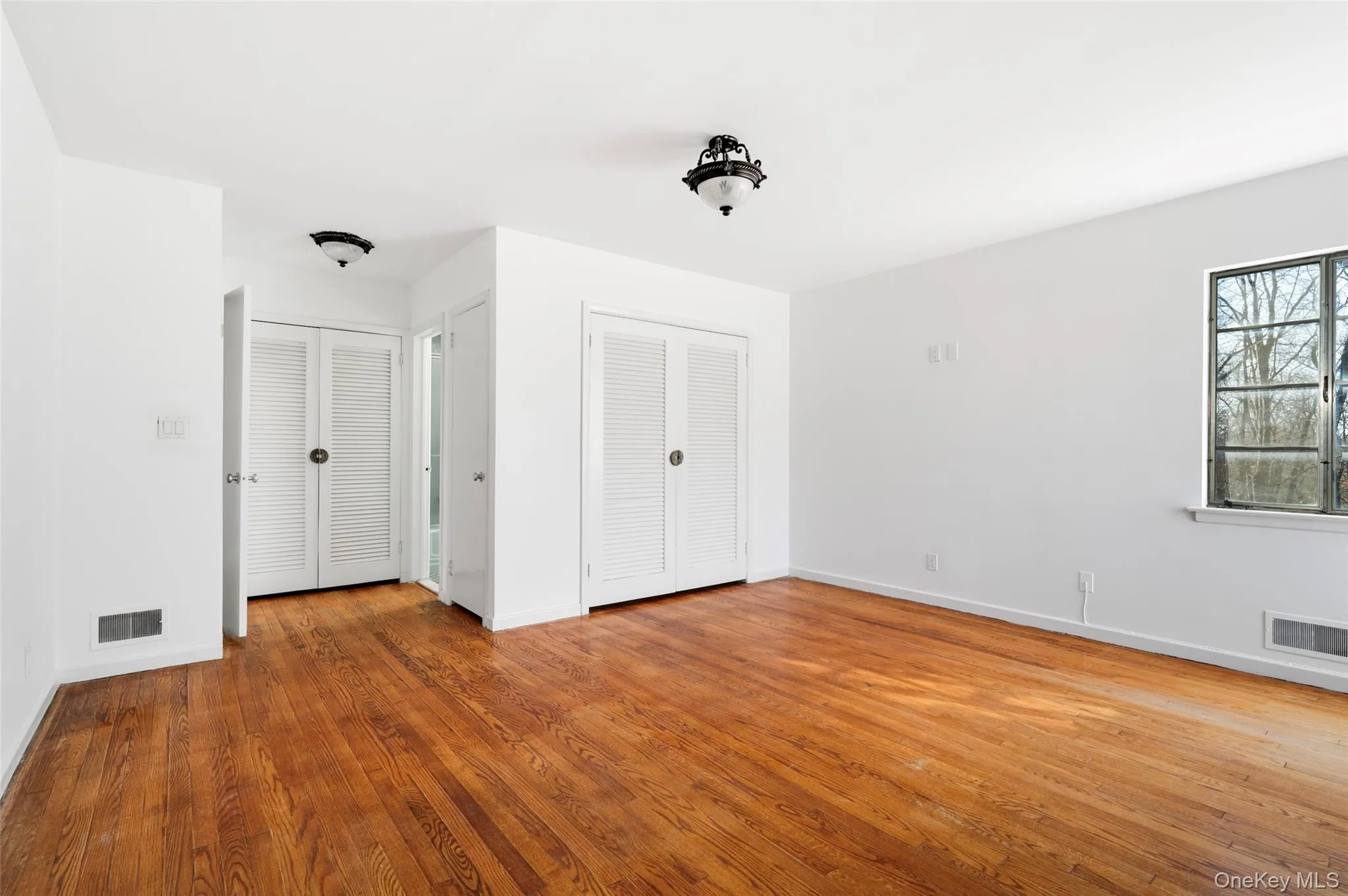 Unfurnished bedroom with multiple closets and hardwood / wood-style flooring Unfurnished bedroom with multiple closets and hardwood / wood-style flooring