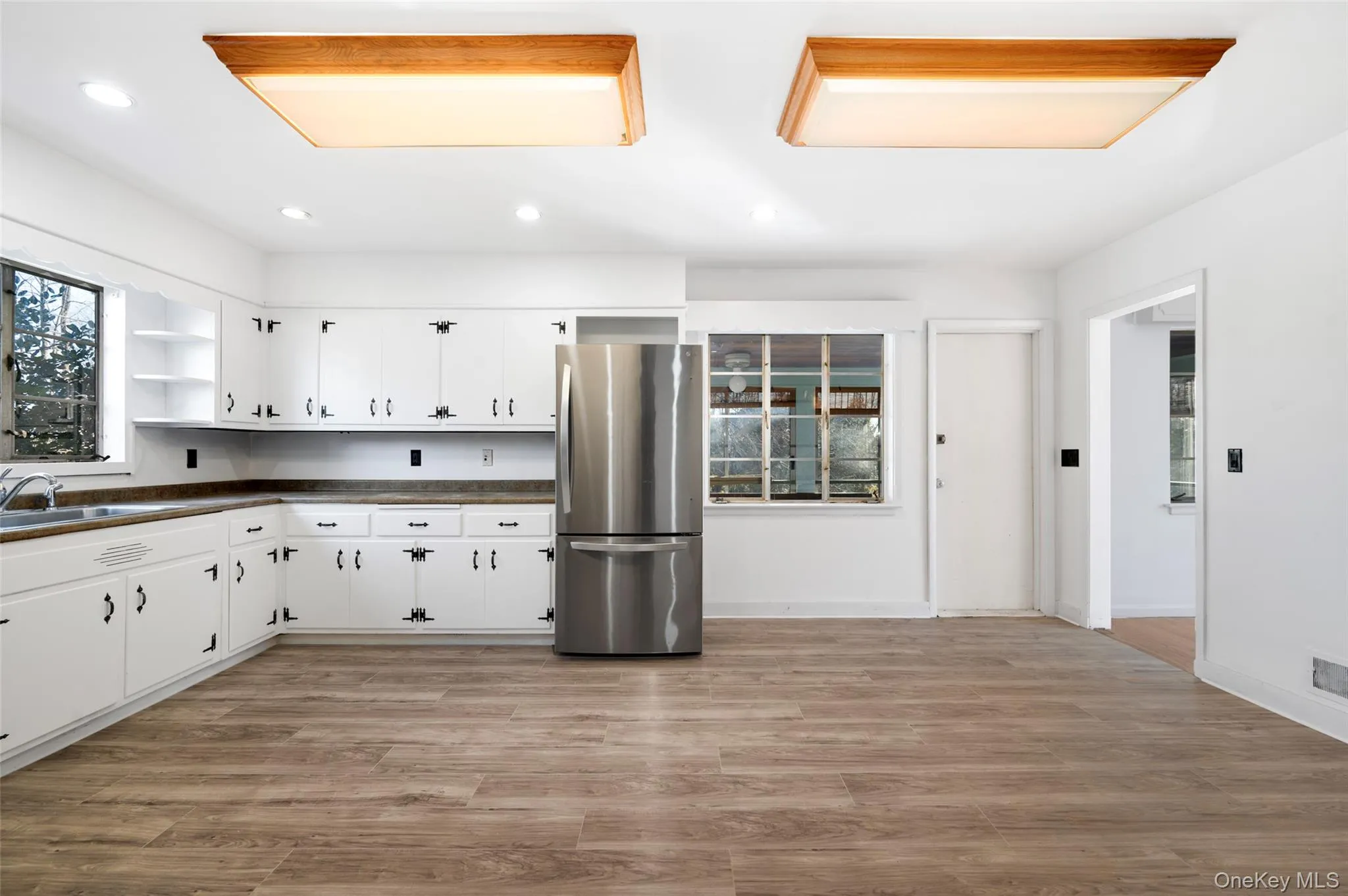 Kitchen with light hardwood / wood-style flooring, white cabinetry, stainless steel refrigerator, and sink Kitchen with light hardwood / wood-style flooring, white cabinetry, stainless steel refrigerator, and sink