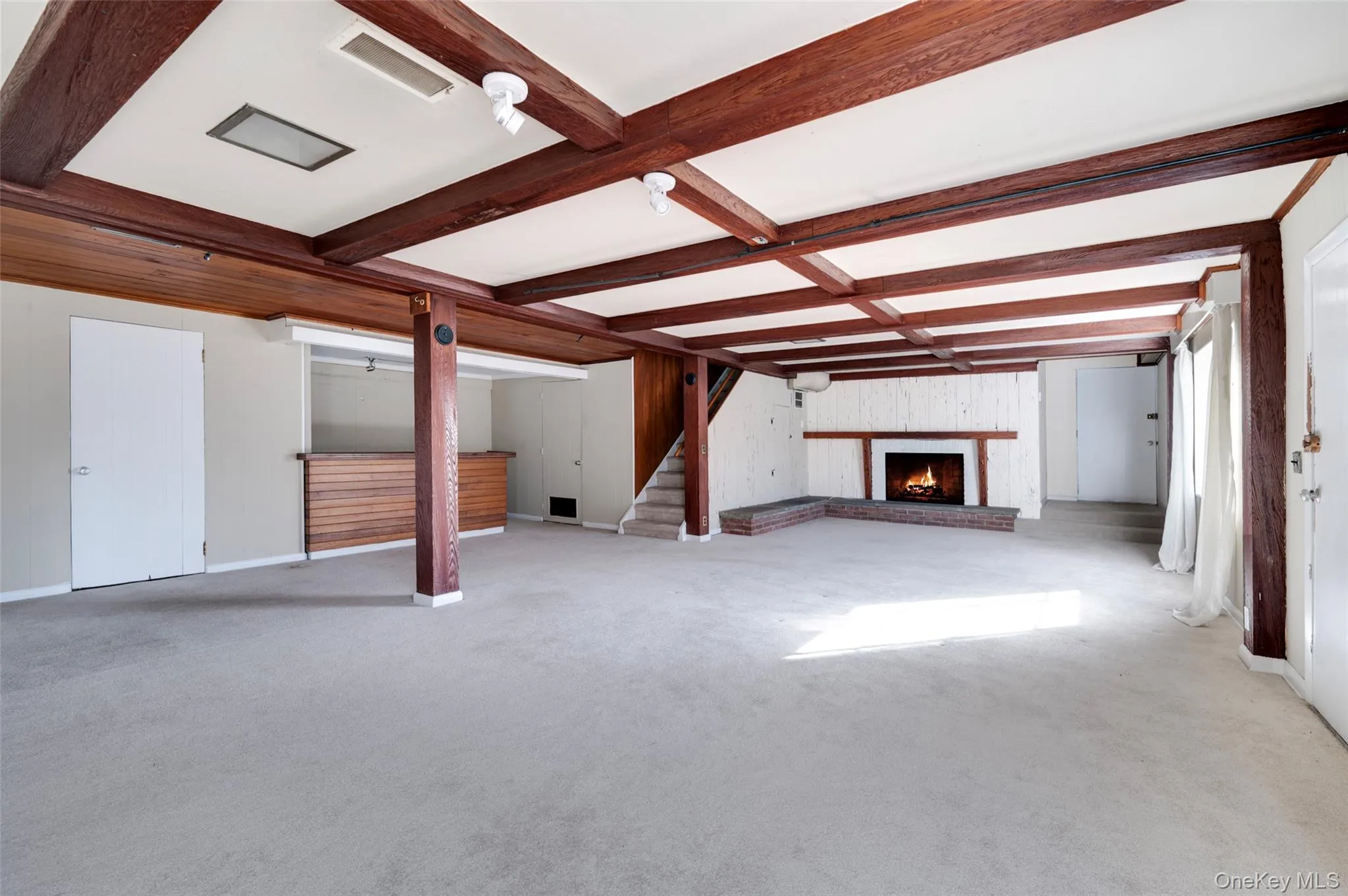 Unfurnished living room featuring beam ceiling, light colored carpet, and a brick fireplace Unfurnished living room featuring beam ceiling, light colored carpet, and a brick fireplace