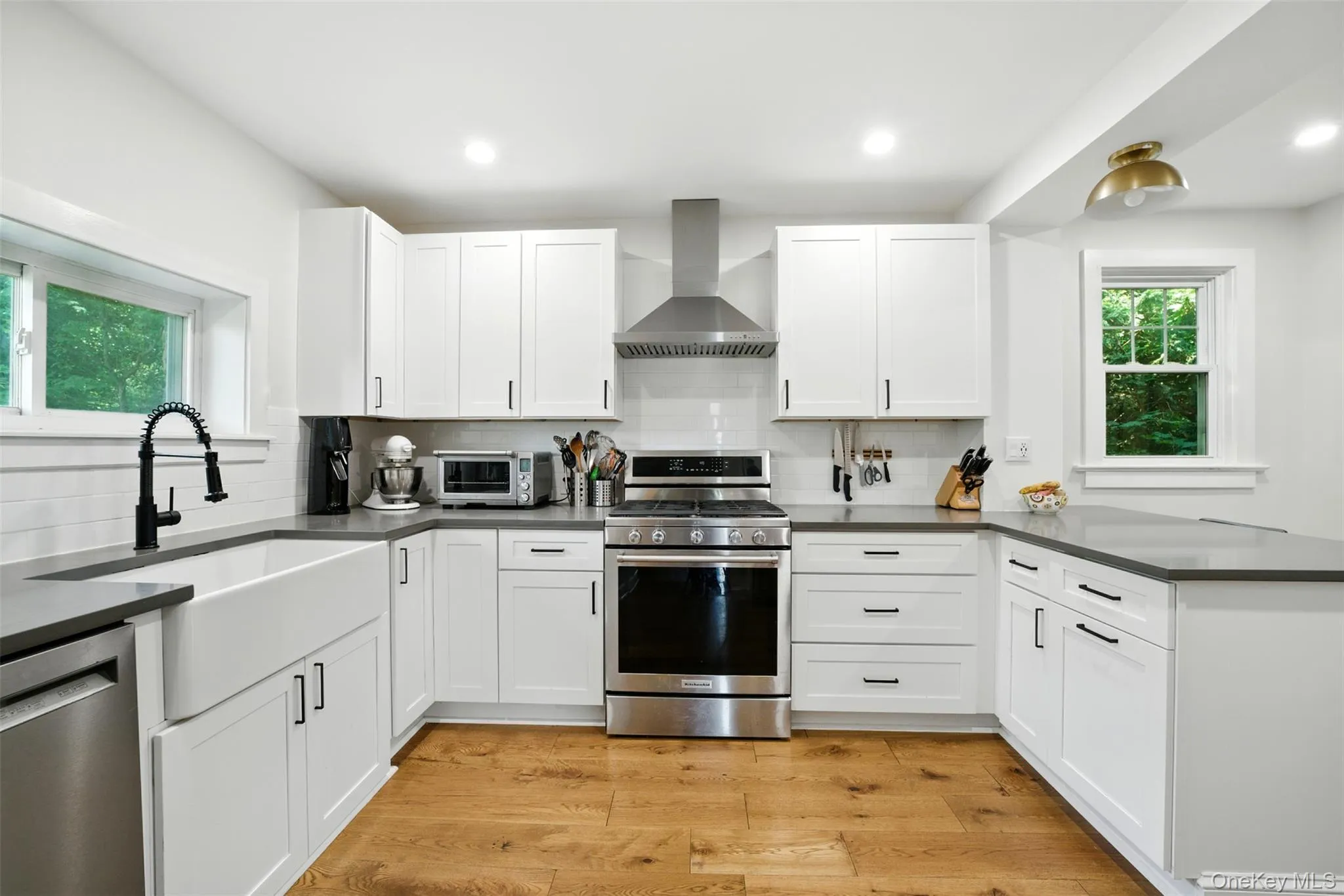 Kitchen with appliances with stainless steel finishes, wall chimney range hood, tasteful backsplash, dark countertops, and white cabinetry Kitchen with appliances with stainless steel finishes, wall chimney range hood, tasteful backsplash, dark countertops, and white cabinetry