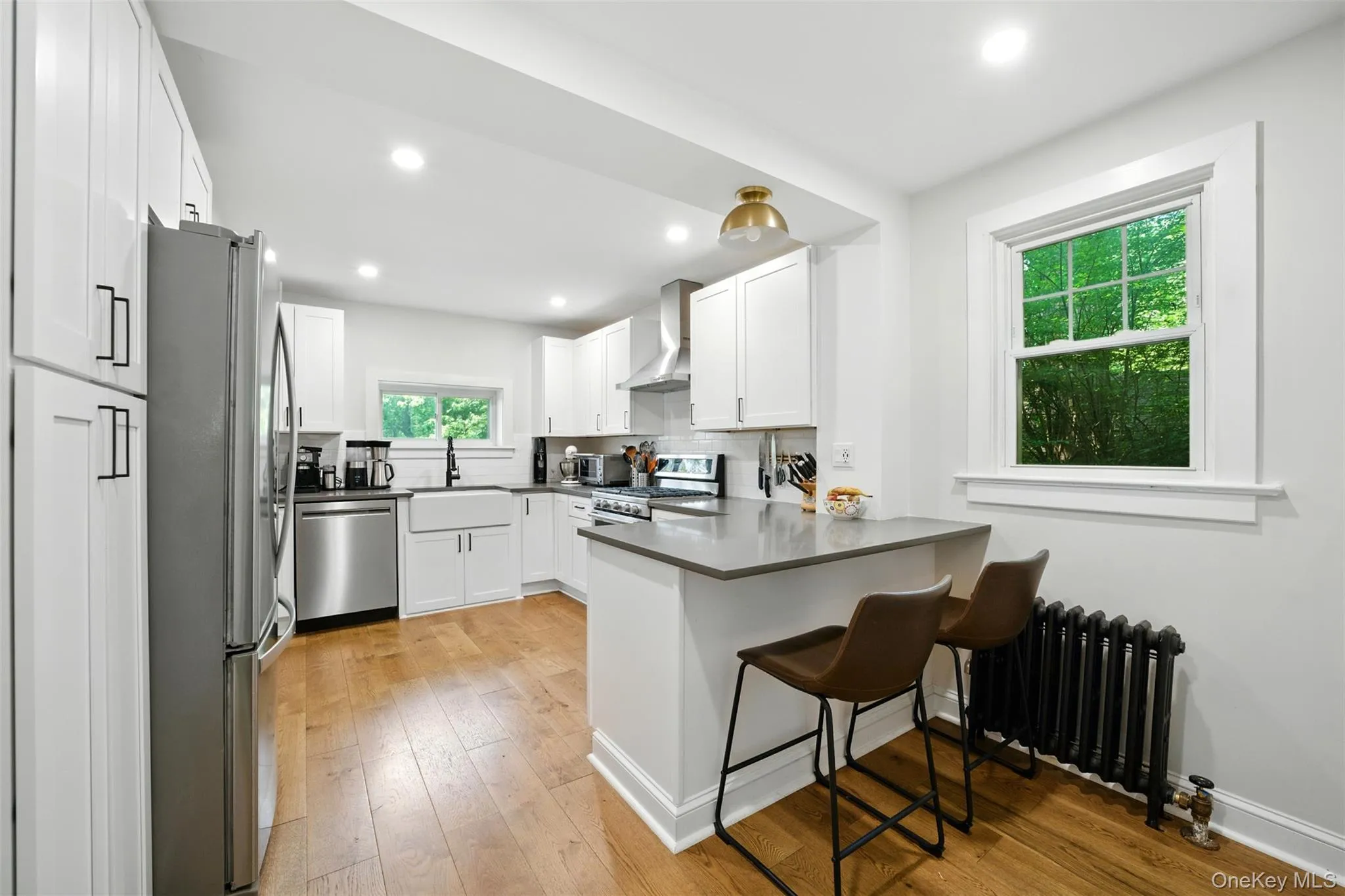 Kitchen with stainless steel appliances, radiator, wall chimney range hood, a peninsula, and white cabinets Kitchen with stainless steel appliances, radiator, wall chimney range hood, a peninsula, and white cabinets