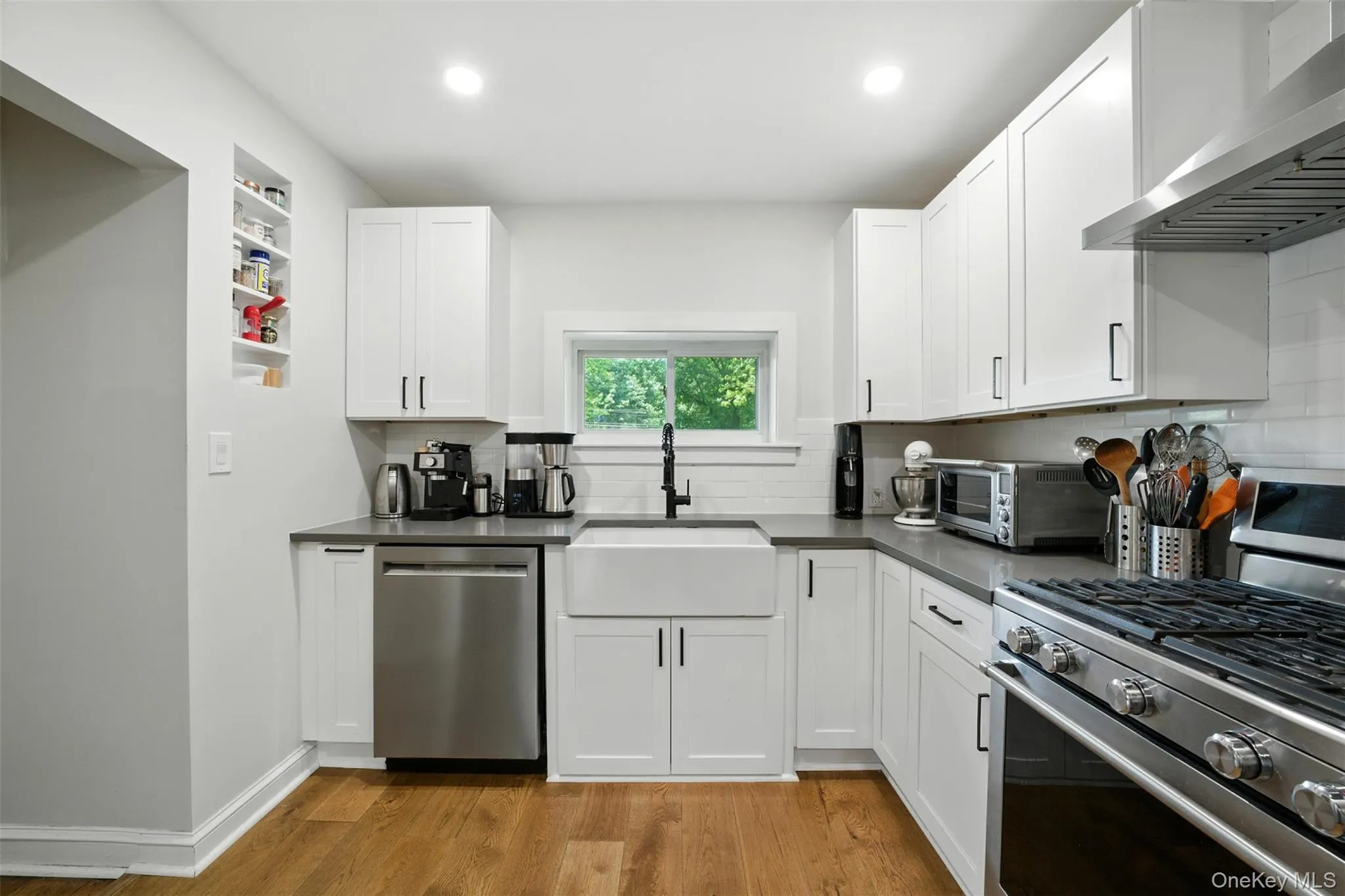 Kitchen with stainless steel appliances, wall chimney range hood, light wood-style floors, tasteful backsplash, and recessed lighting Kitchen with stainless steel appliances, wall chimney range hood, light wood-style floors, tasteful backsplash, and recessed lighting