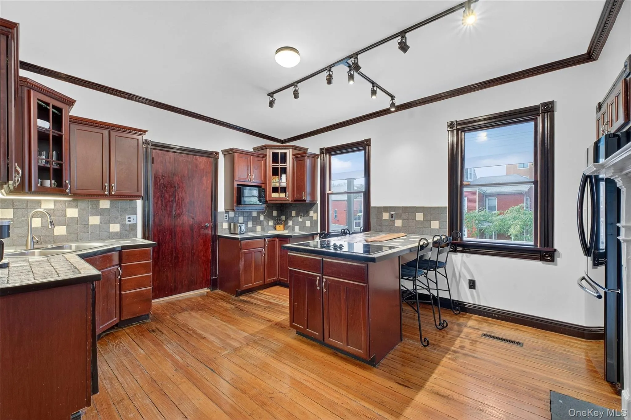 Kitchen featuring track lighting, ornamental molding, light wood-style flooring, tasteful backsplash, and glass insert cabinets Kitchen featuring track lighting, ornamental molding, light wood-style flooring, tasteful backsplash, and glass insert cabinets