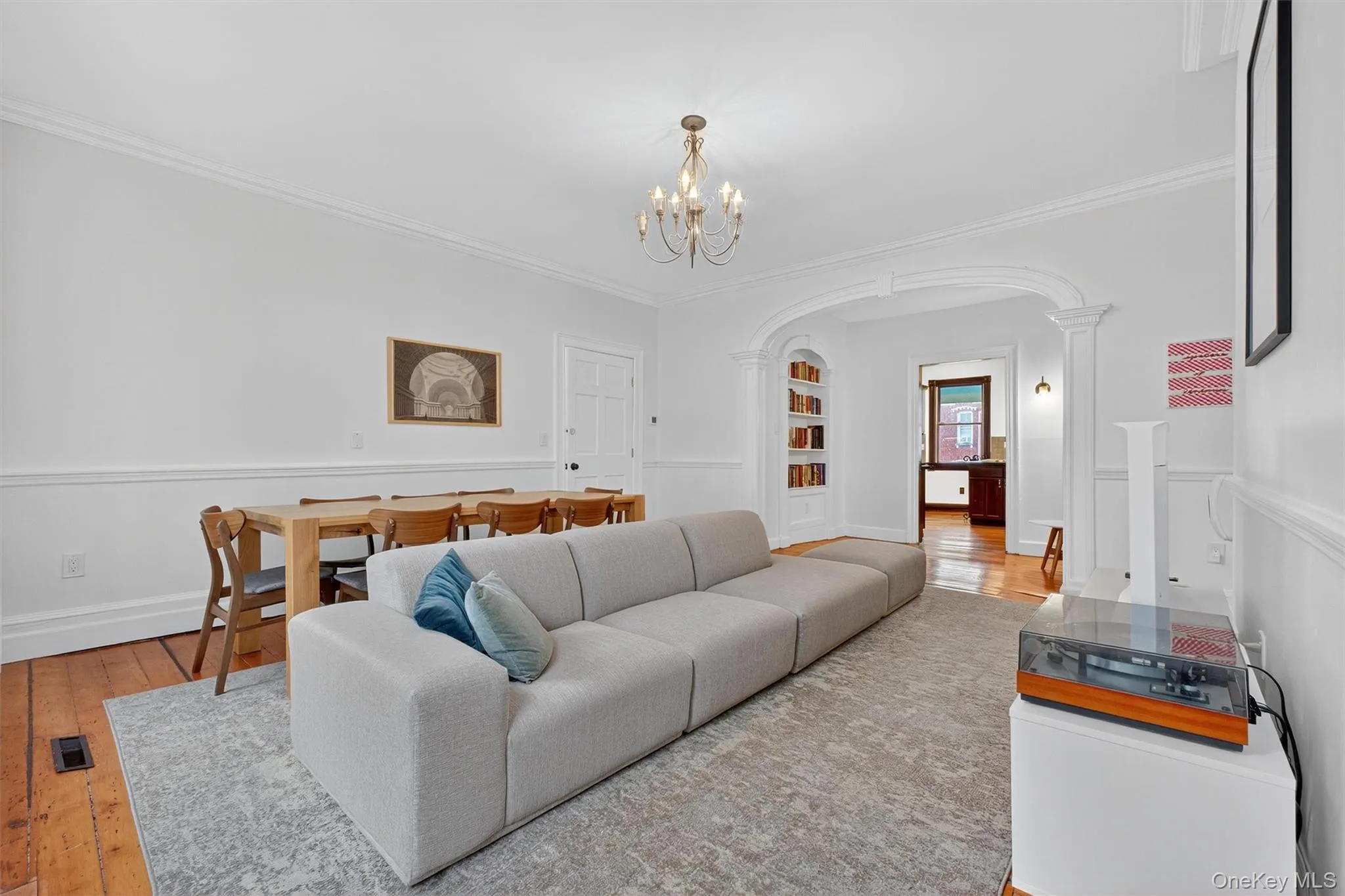 Living area featuring arched walkways, hardwood / wood-style floors, ornamental molding, built in shelves, and a chandelier Living area featuring arched walkways, hardwood / wood-style floors, ornamental molding, built in shelves, and a chandelier