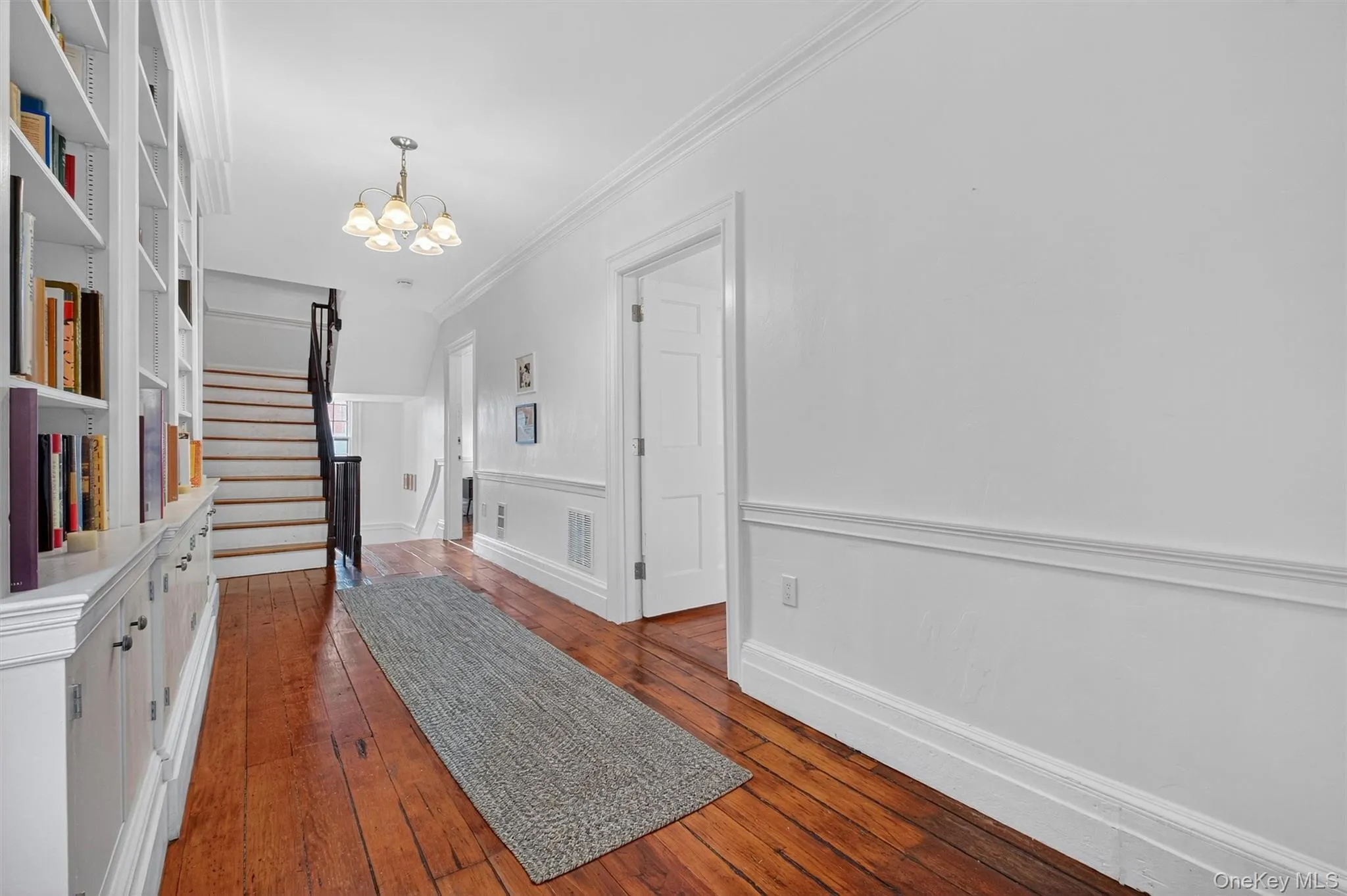 Corridor featuring hardwood / wood-style flooring, crown molding, a chandelier, and stairway Corridor featuring hardwood / wood-style flooring, crown molding, a chandelier, and stairway