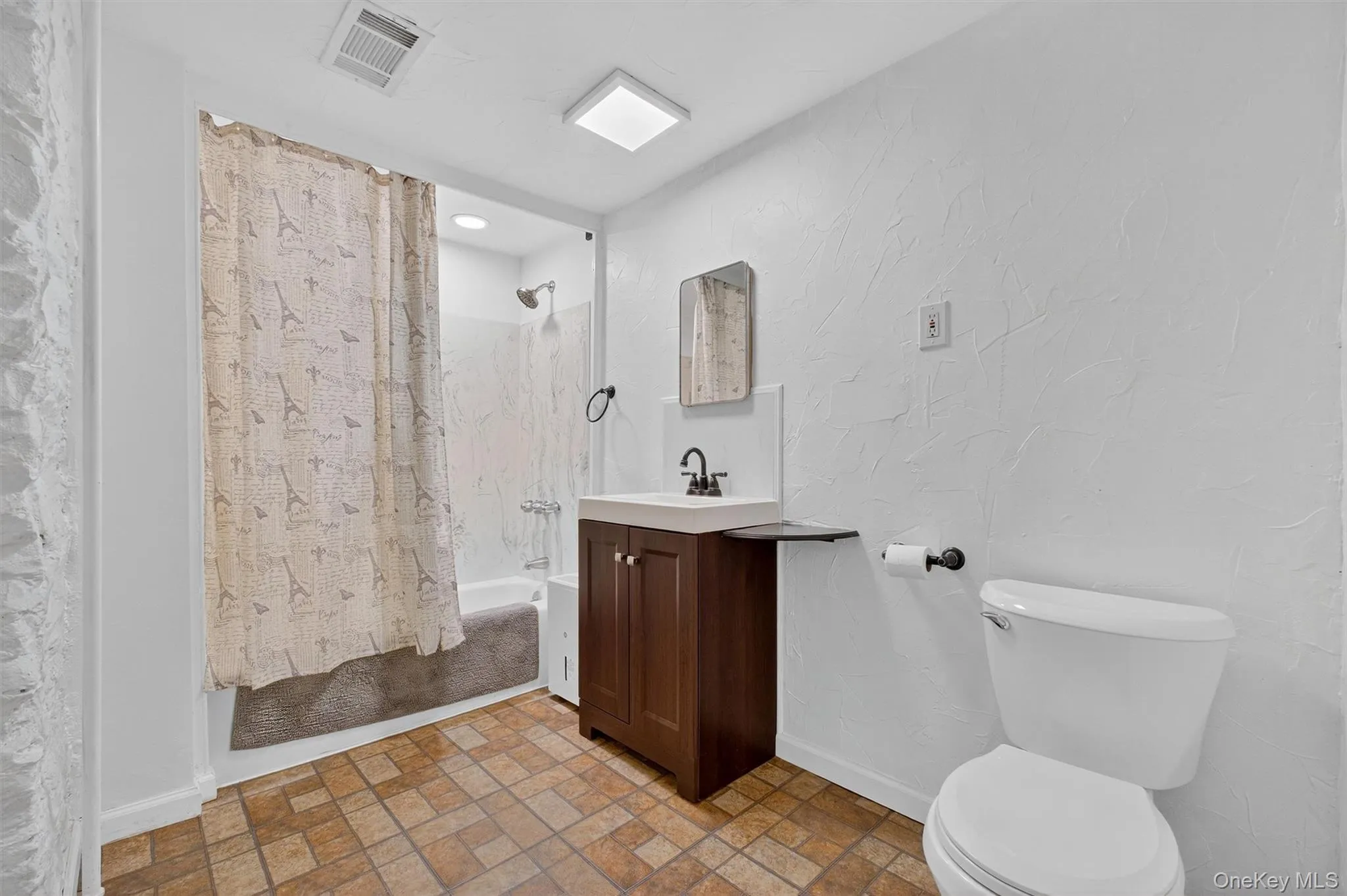 Full bath featuring vanity, shower / bath combo with shower curtain, brick patterned flooring, and a textured wall Full bath featuring vanity, shower / bath combo with shower curtain, brick patterned flooring, and a textured wall