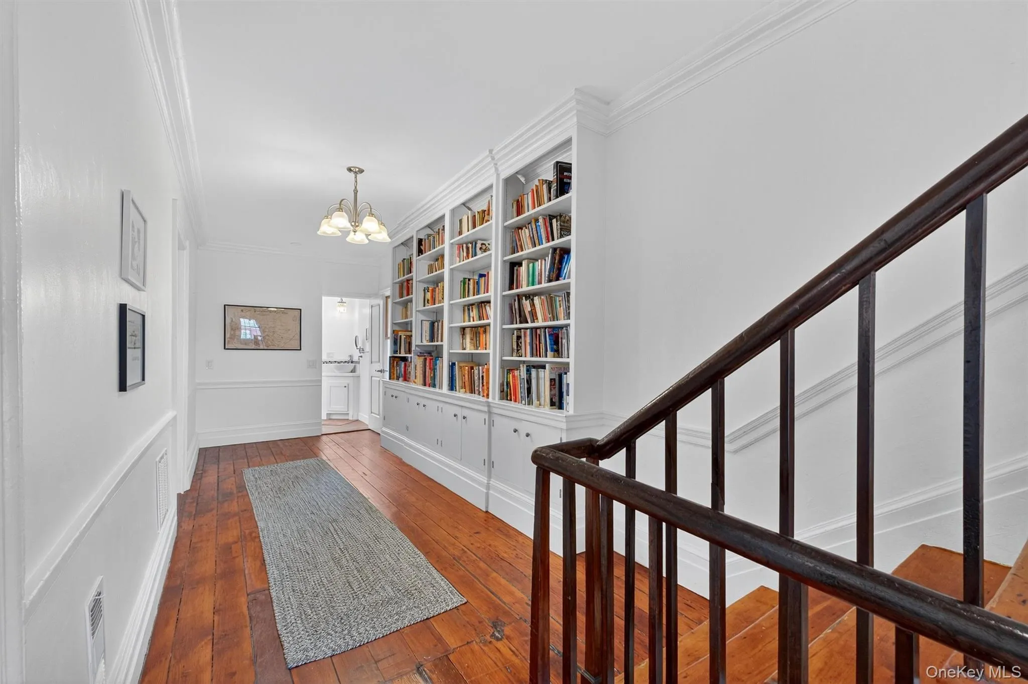 Hallway featuring hardwood / wood-style flooring, ornamental molding, stairway, a chandelier, and built in shelves Hallway featuring hardwood / wood-style flooring, ornamental molding, stairway, a chandelier, and built in shelves
