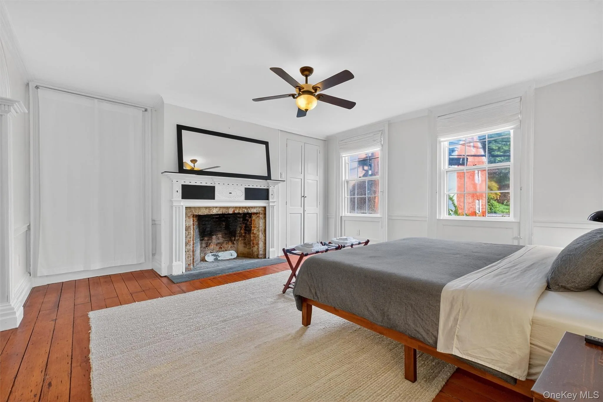 Bedroom featuring wood-type flooring, a decorative wall, a fireplace, a ceiling fan, and ornamental molding Bedroom featuring wood-type flooring, a decorative wall, a fireplace, a ceiling fan, and ornamental molding